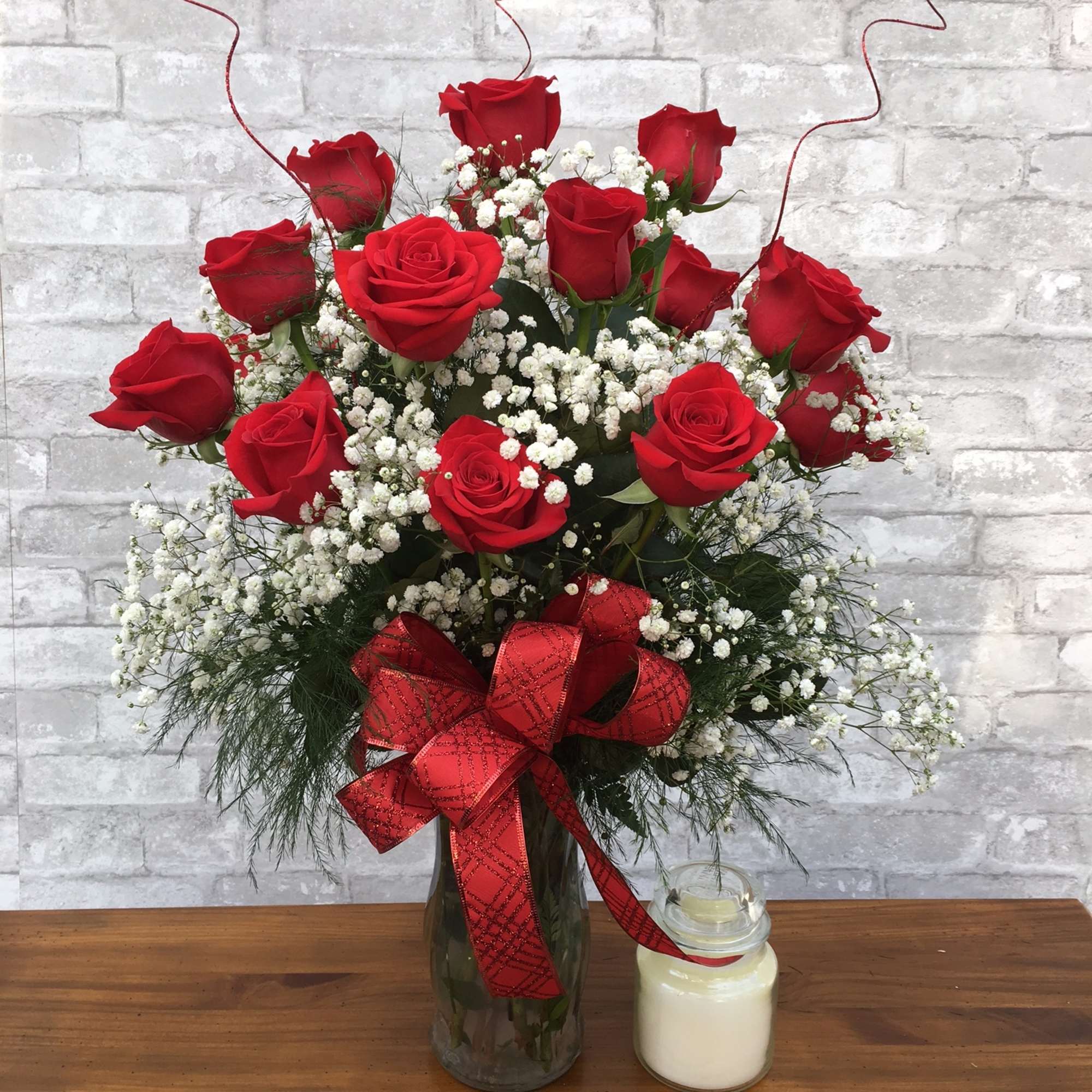 Red roses in a glass vase with baby's breath and a red ribbon