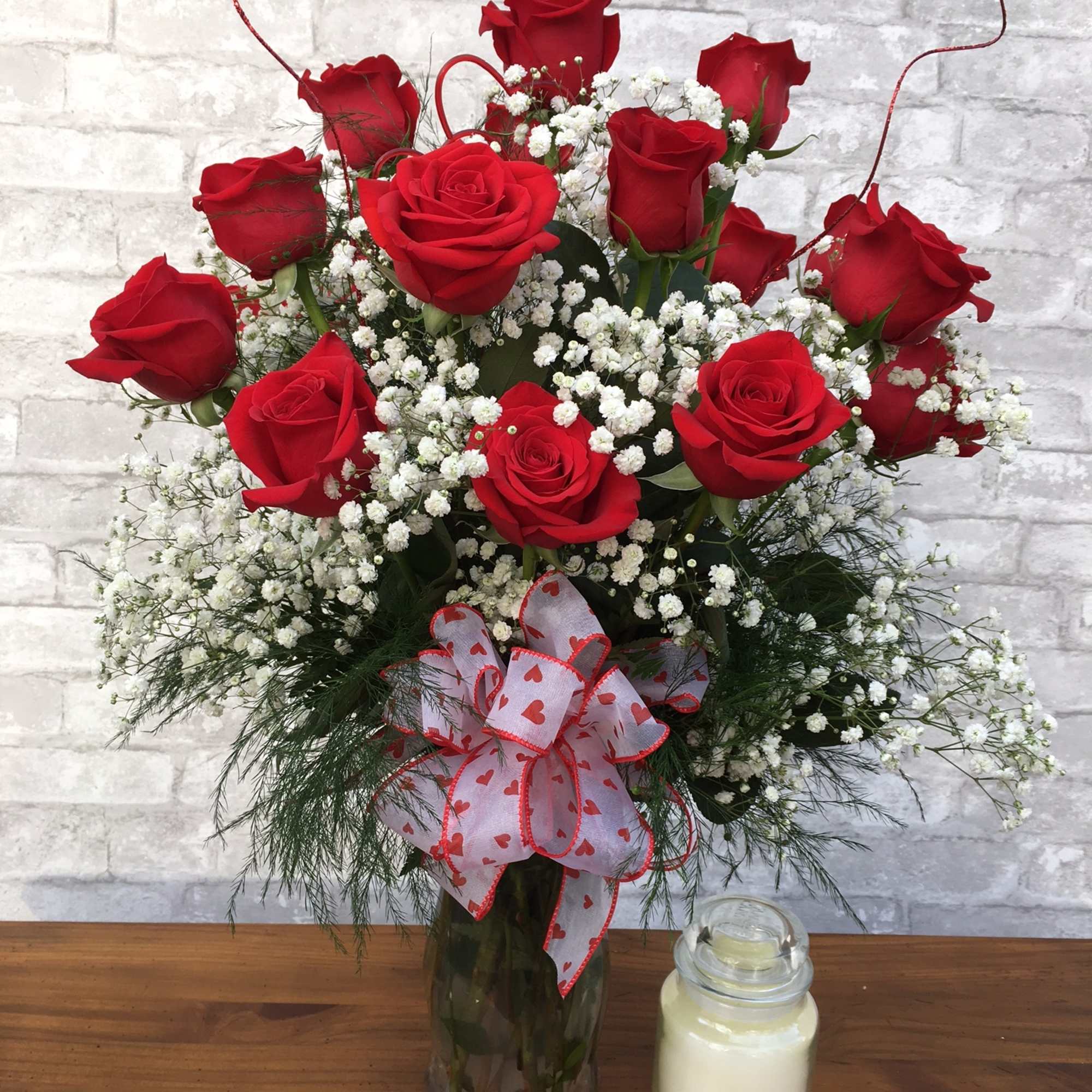 Red roses in a glass vase with baby's breath and a heart ribbon