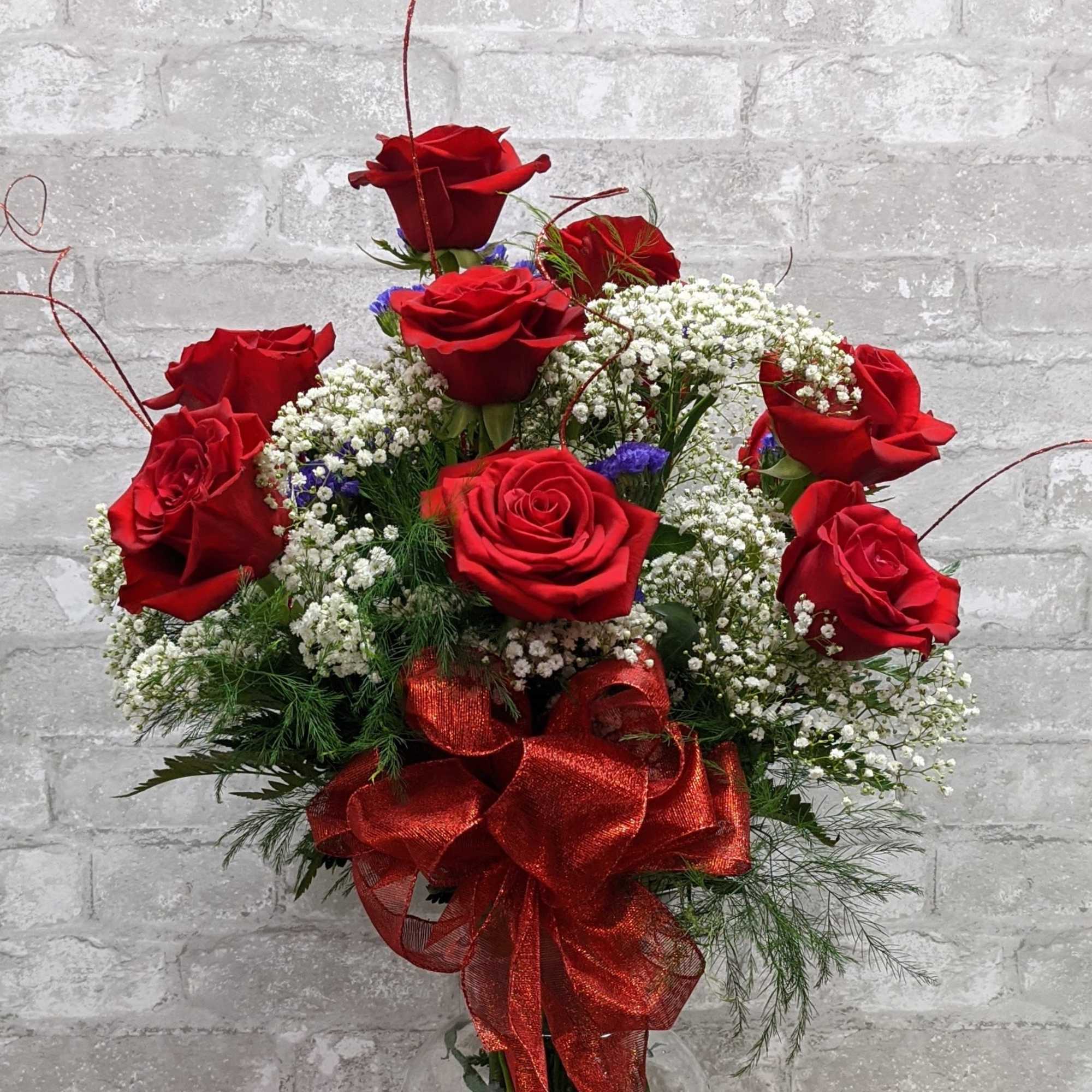 Red roses arranged in a clear glass vase with a red ribbon bow