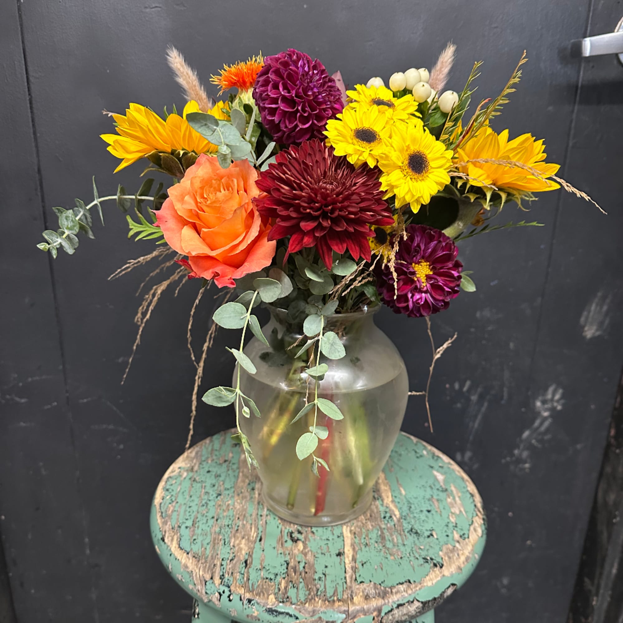 Mixed bouquet in a clear glass vase with yellow, orange, and burgundy blooms