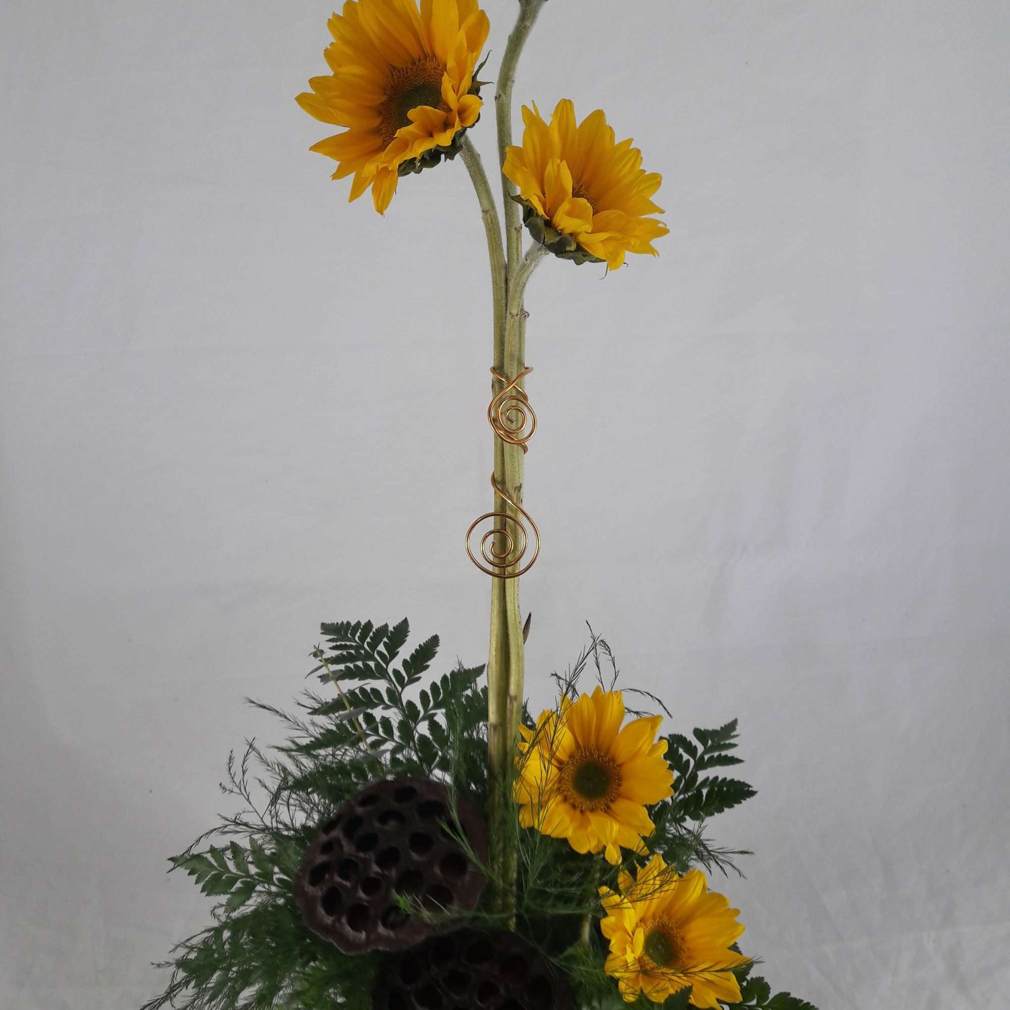 Tall arrangement of yellow sunflowers with fern and lotus pods
