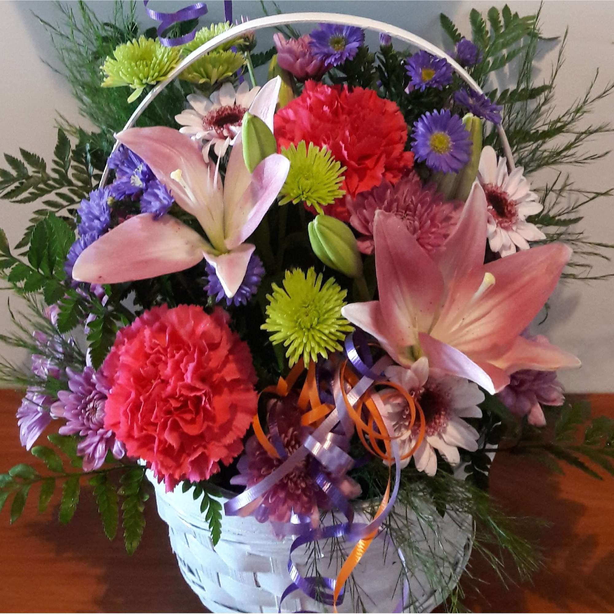 Mixed bouquet with pink lilies, carnations, and purple daisies in a white basket