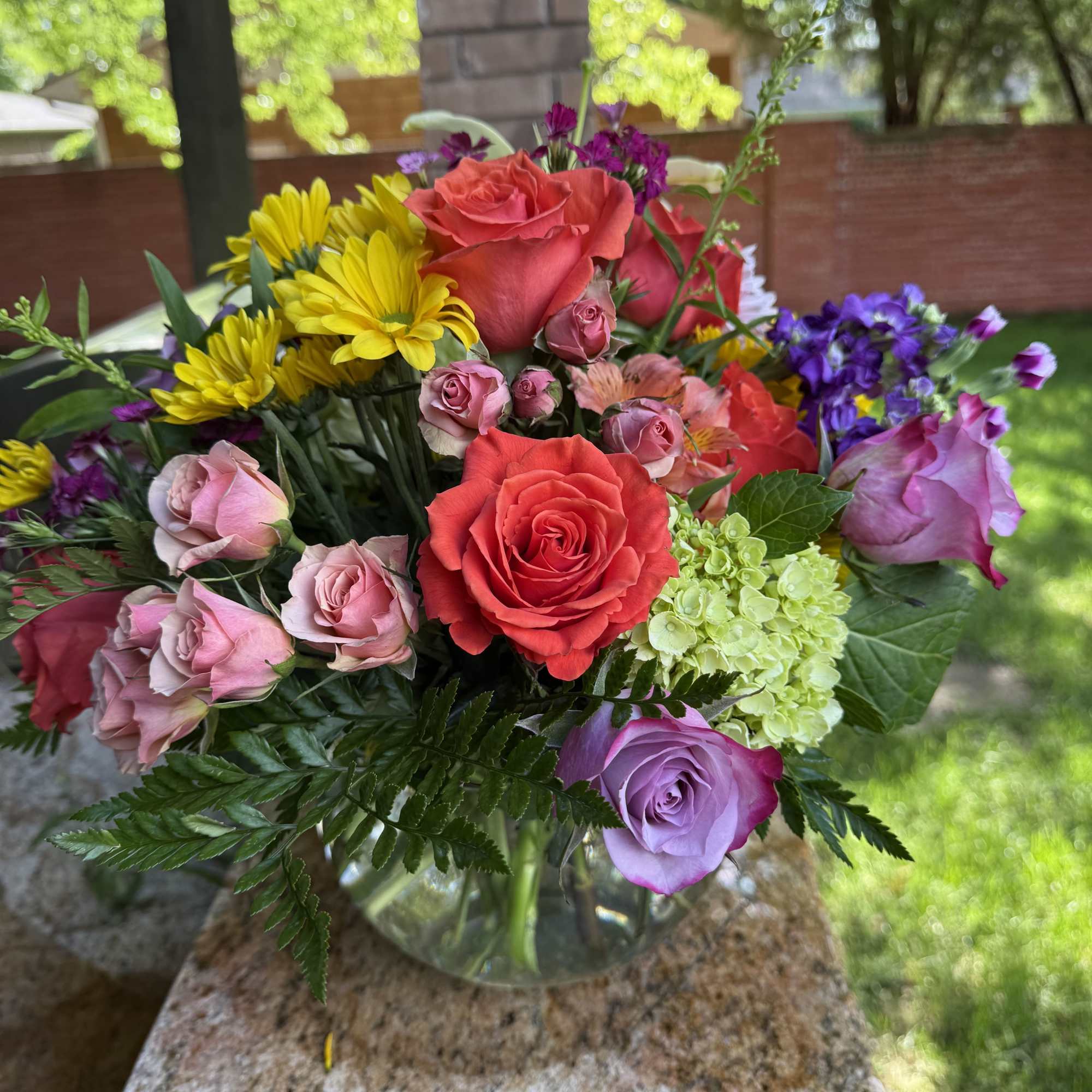 Mixed bouquet of roses, yellow daisies, and hydrangea in a glass vase