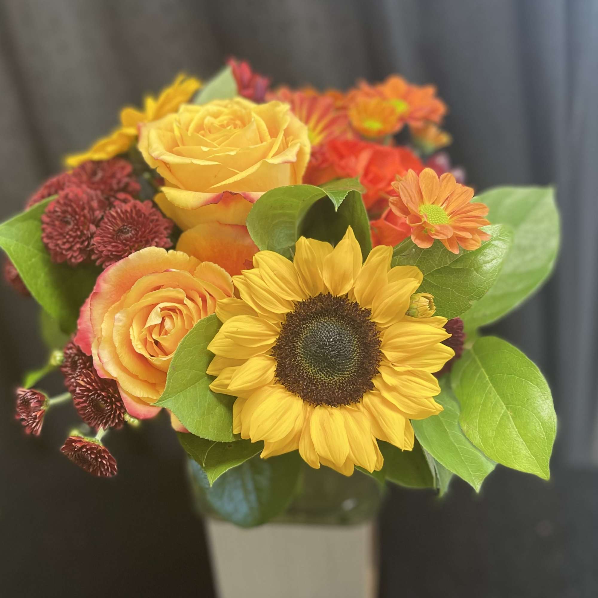 Mixed bouquet with yellow roses, a sunflower, and orange daisies in a vase