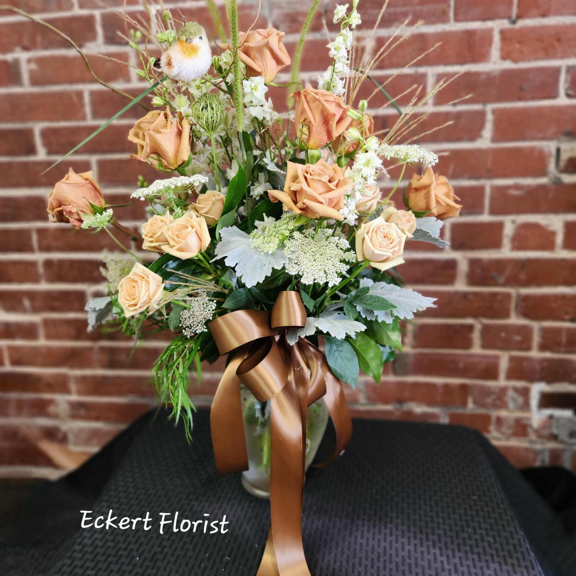 Peach roses arranged in a clear vase with a brown ribbon