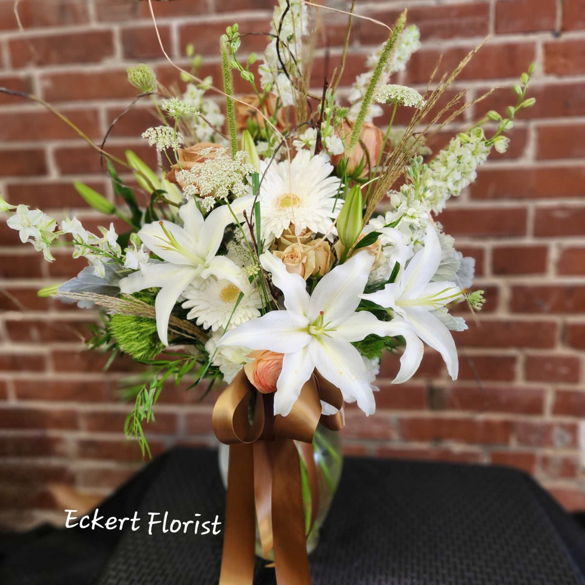 White lilies and daisies in a glass vase with a brown ribbon