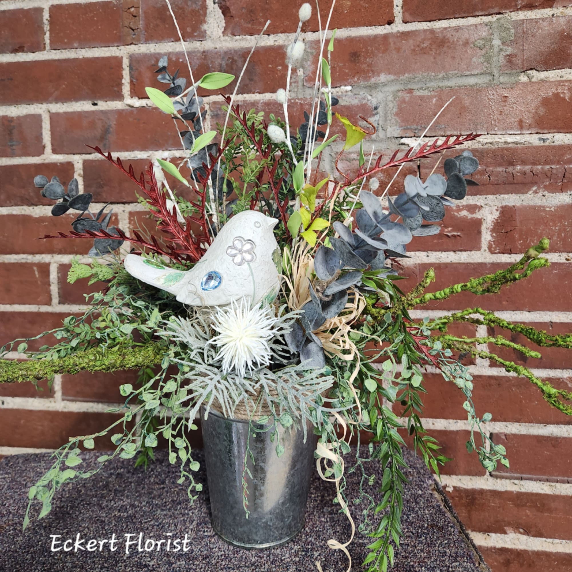Mixed greenery arrangement in a metal vase with a white bird figurine