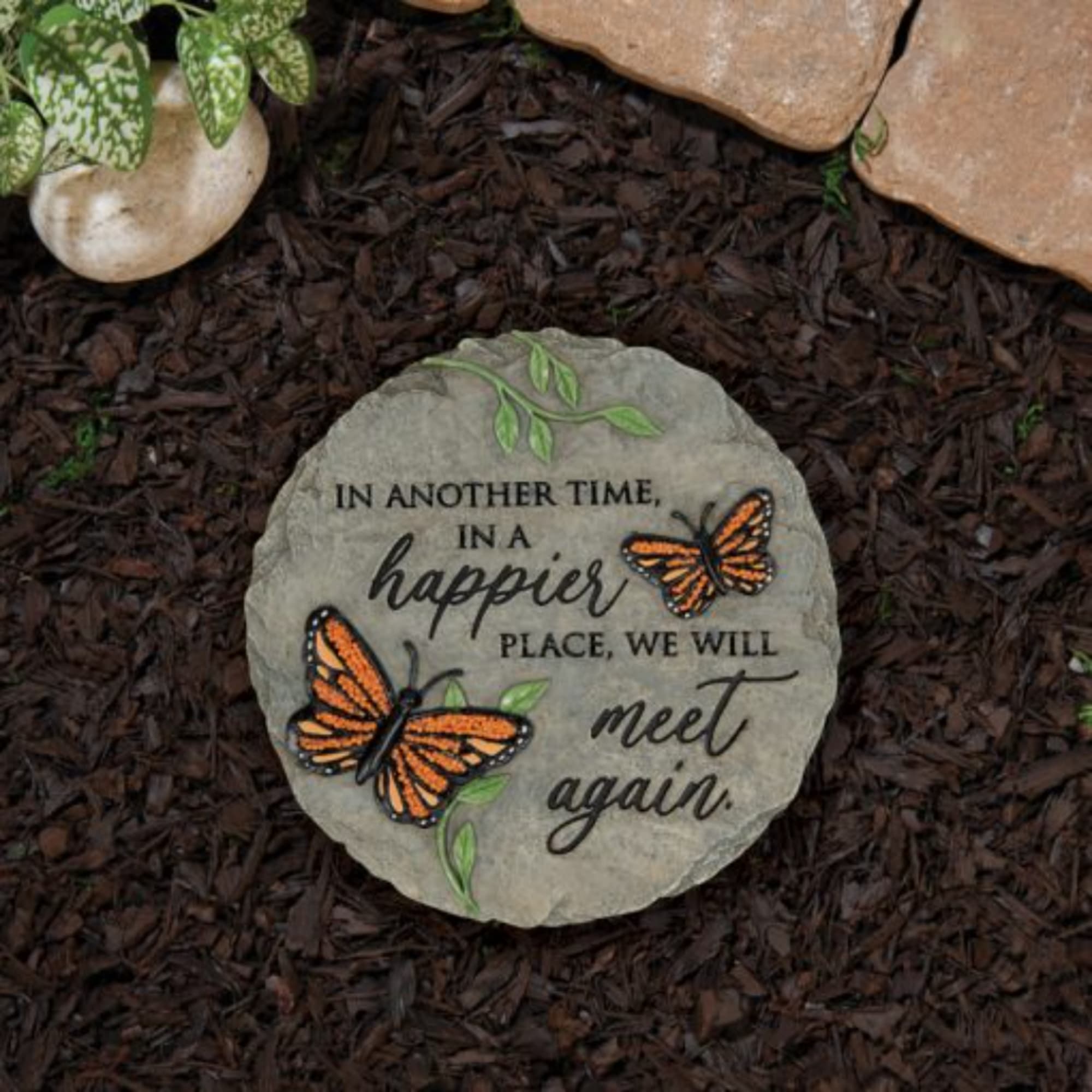 Memorial stone with butterflies and the words "meet again" in a garden bed