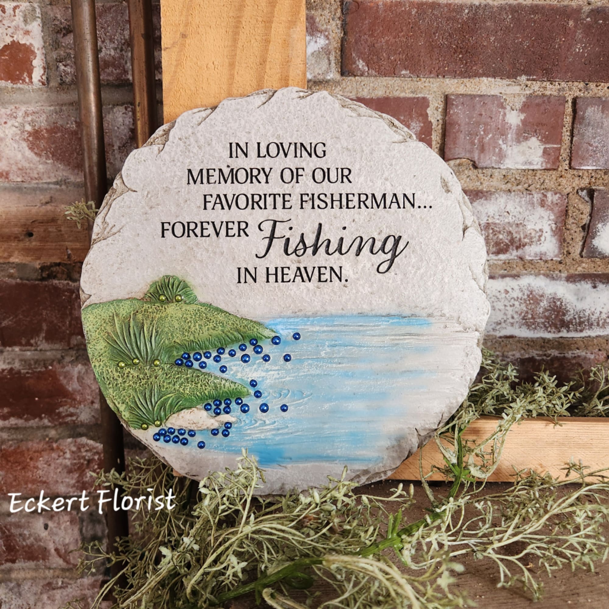 Round memorial stone plaque with fishing-themed text and painted fish