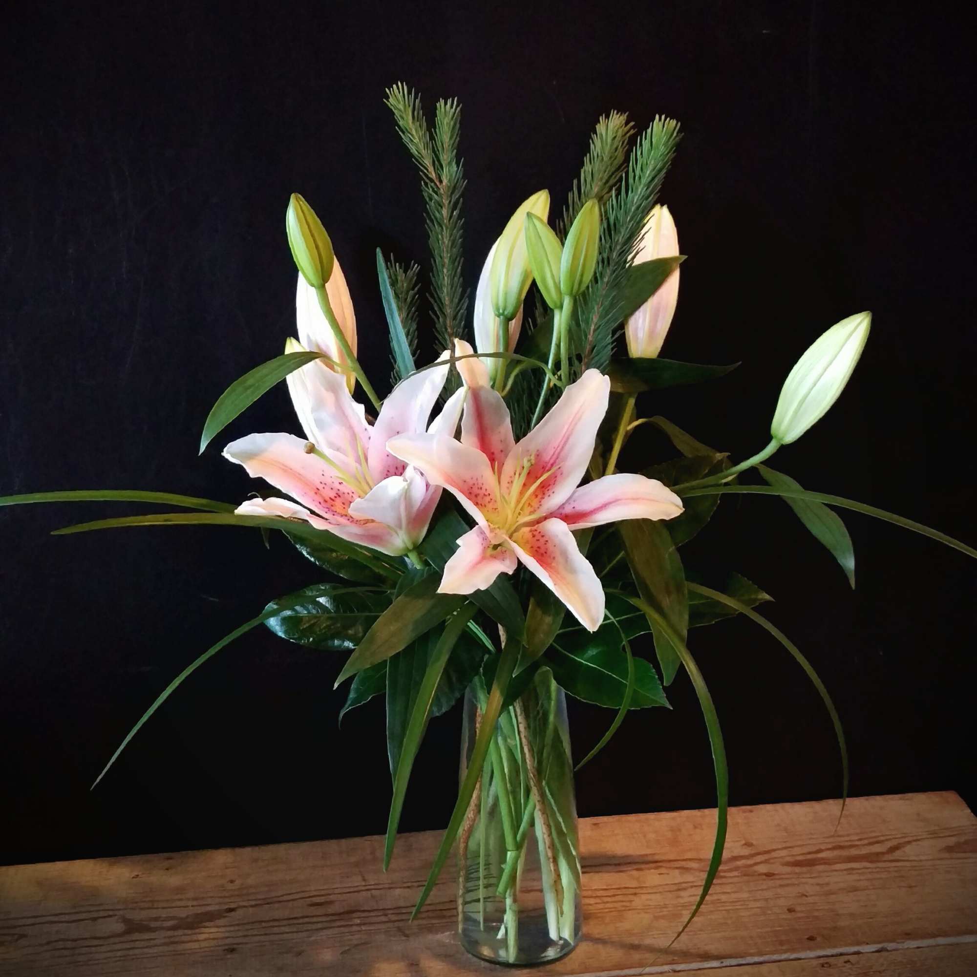 Pink lilies in a clear glass vase with long greenery