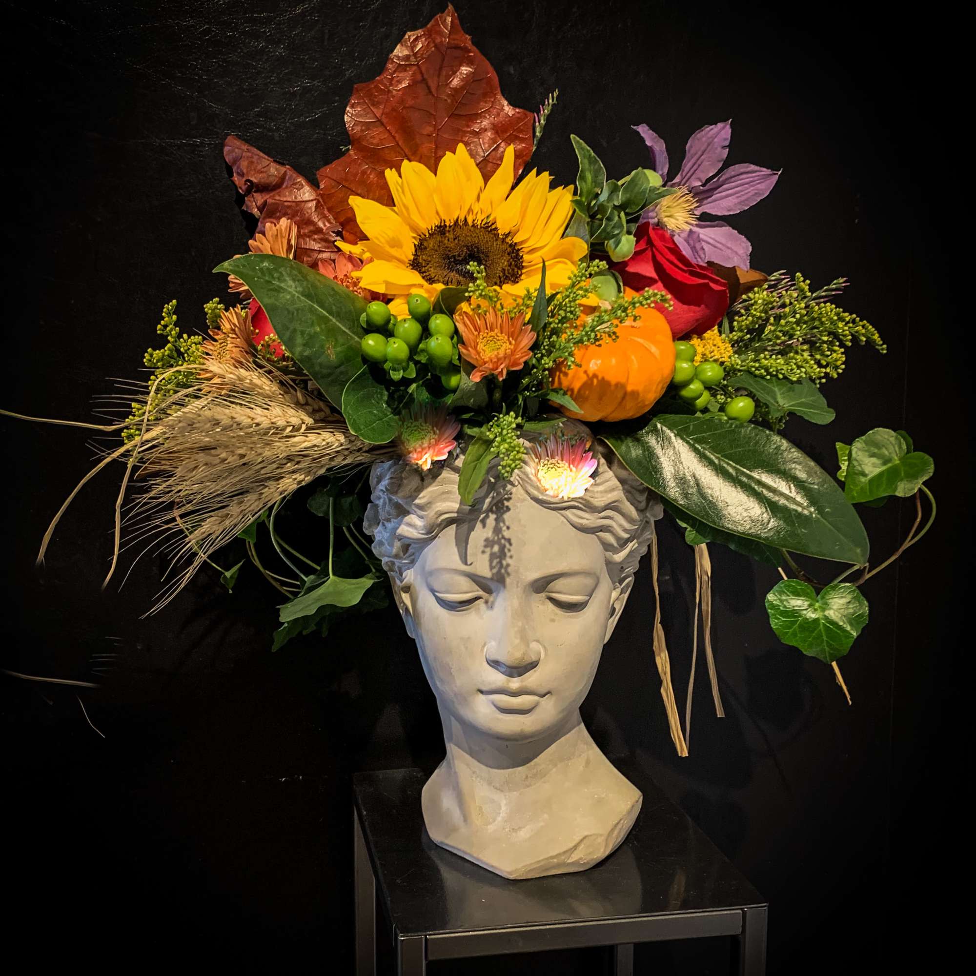 Autumn floral arrangement in a sculpted head vase with sunflower and pumpkin accents