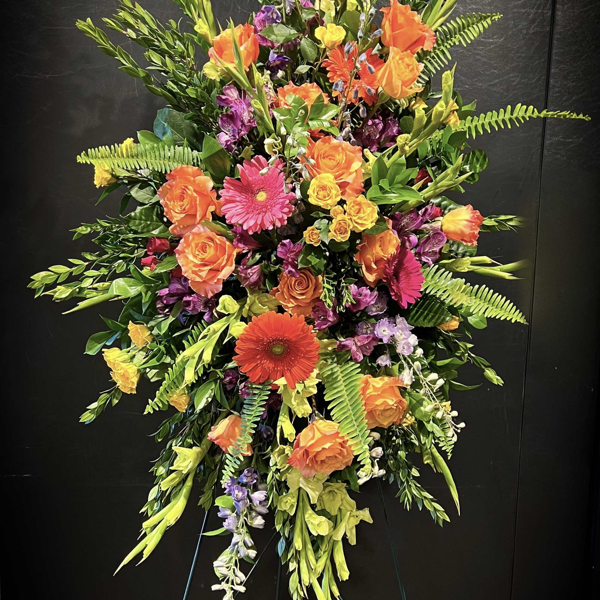 Tall standing spray of orange, yellow, pink, and purple flowers on an easel