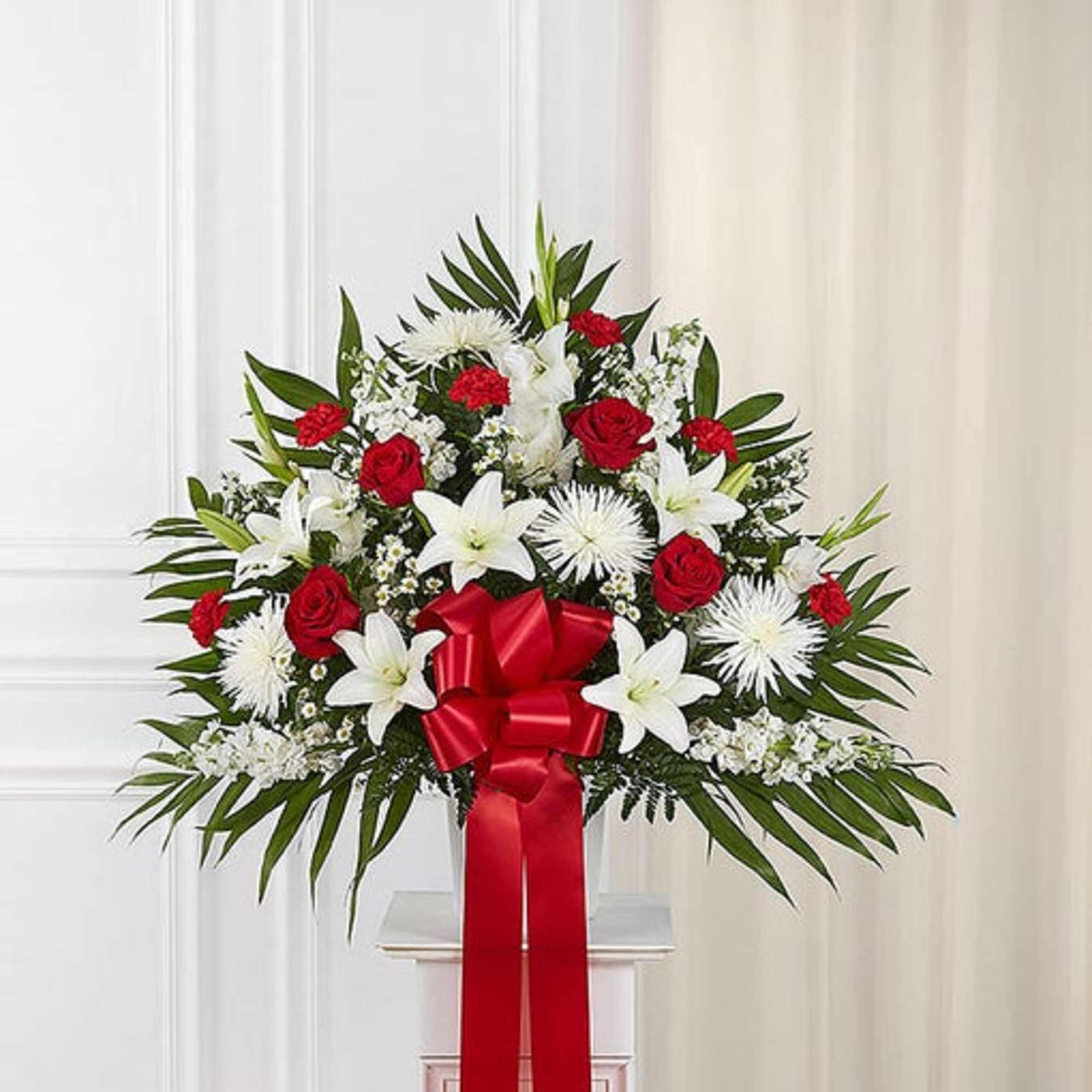 Standing floral spray with red roses, white lilies, and a red ribbon