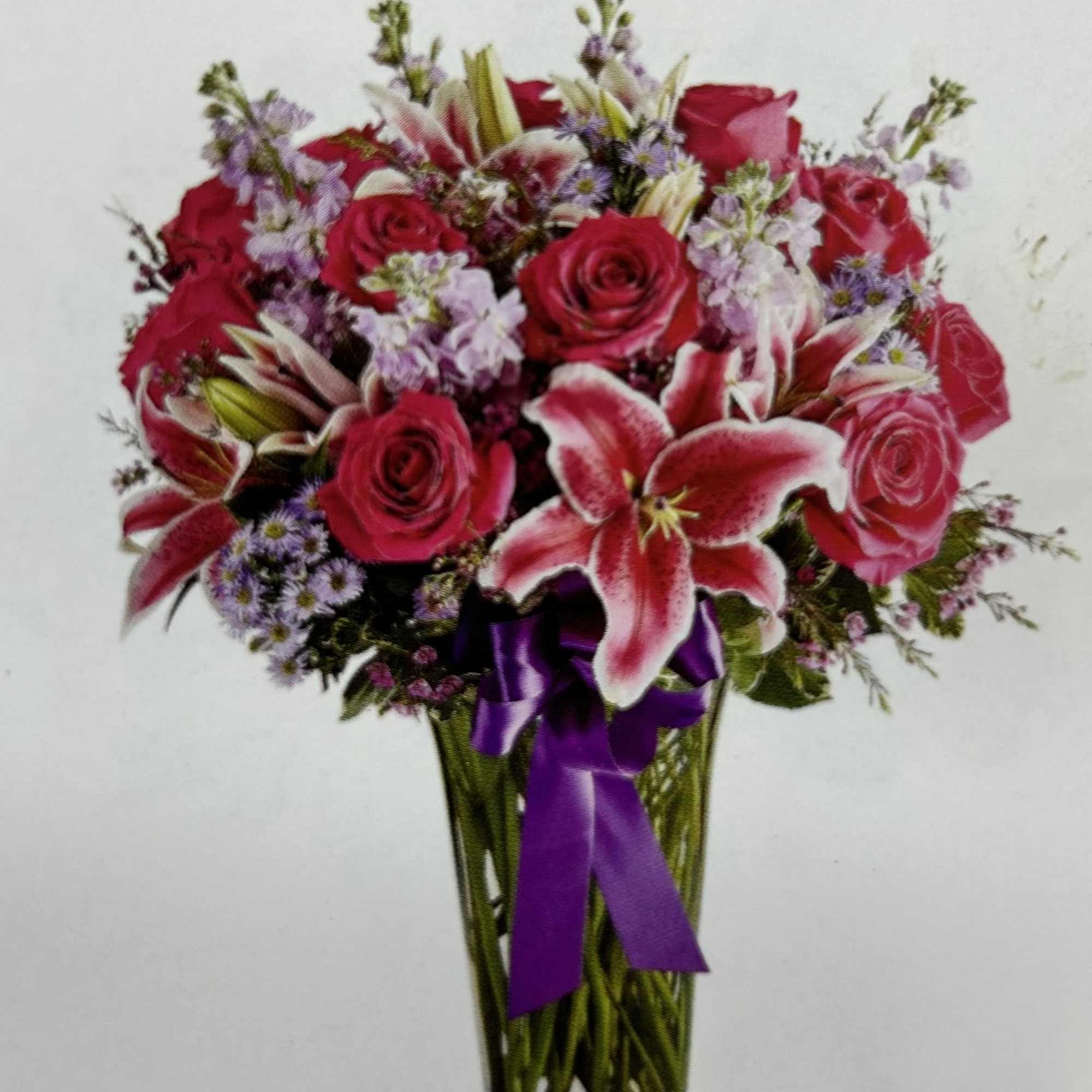 Bouquet of red roses and lilies in a clear glass vase with a purple ribbon