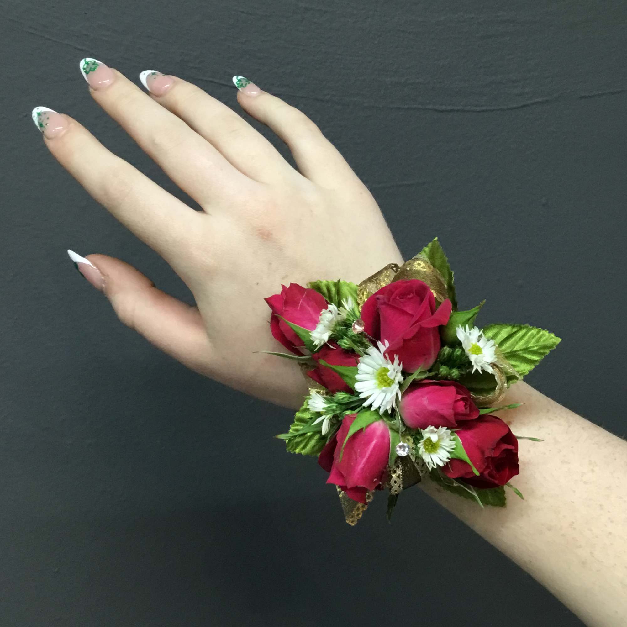 Wrist corsage of red roses and small white flowers on a hand with manicured nails