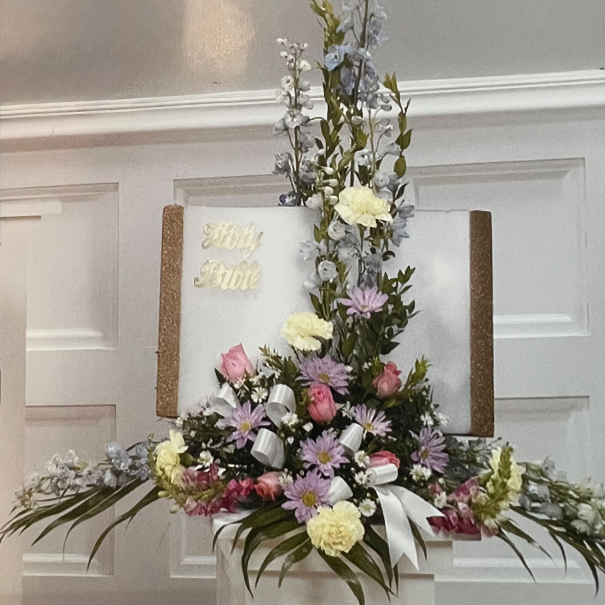 Tall floral arrangement with pink, lavender, and cream flowers on a white board