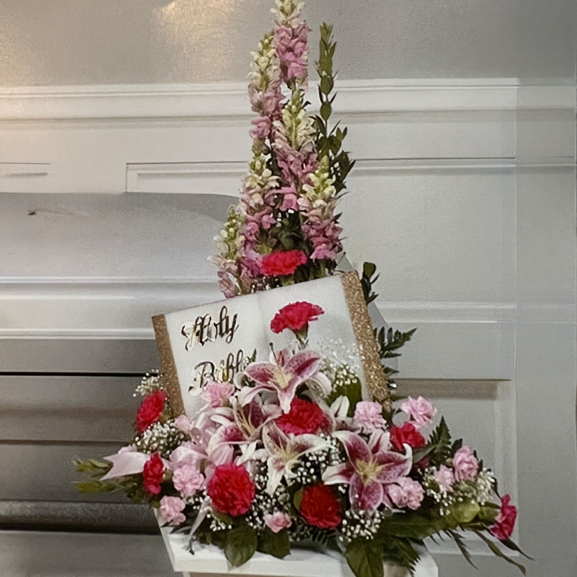 Pink and white floral arrangement with lilies and carnations around a sign