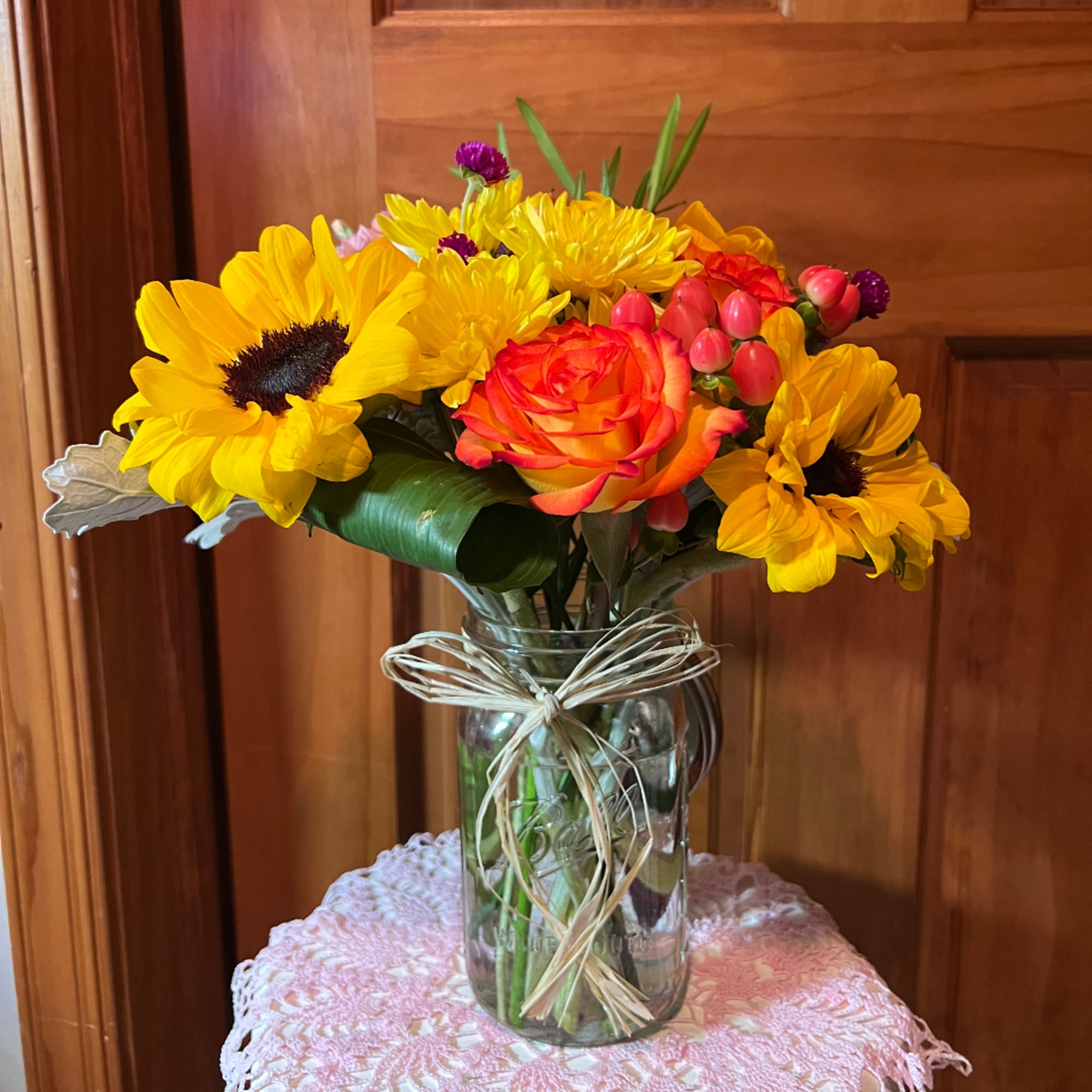 Sunflower and rose bouquet in a glass jar vase with a bow