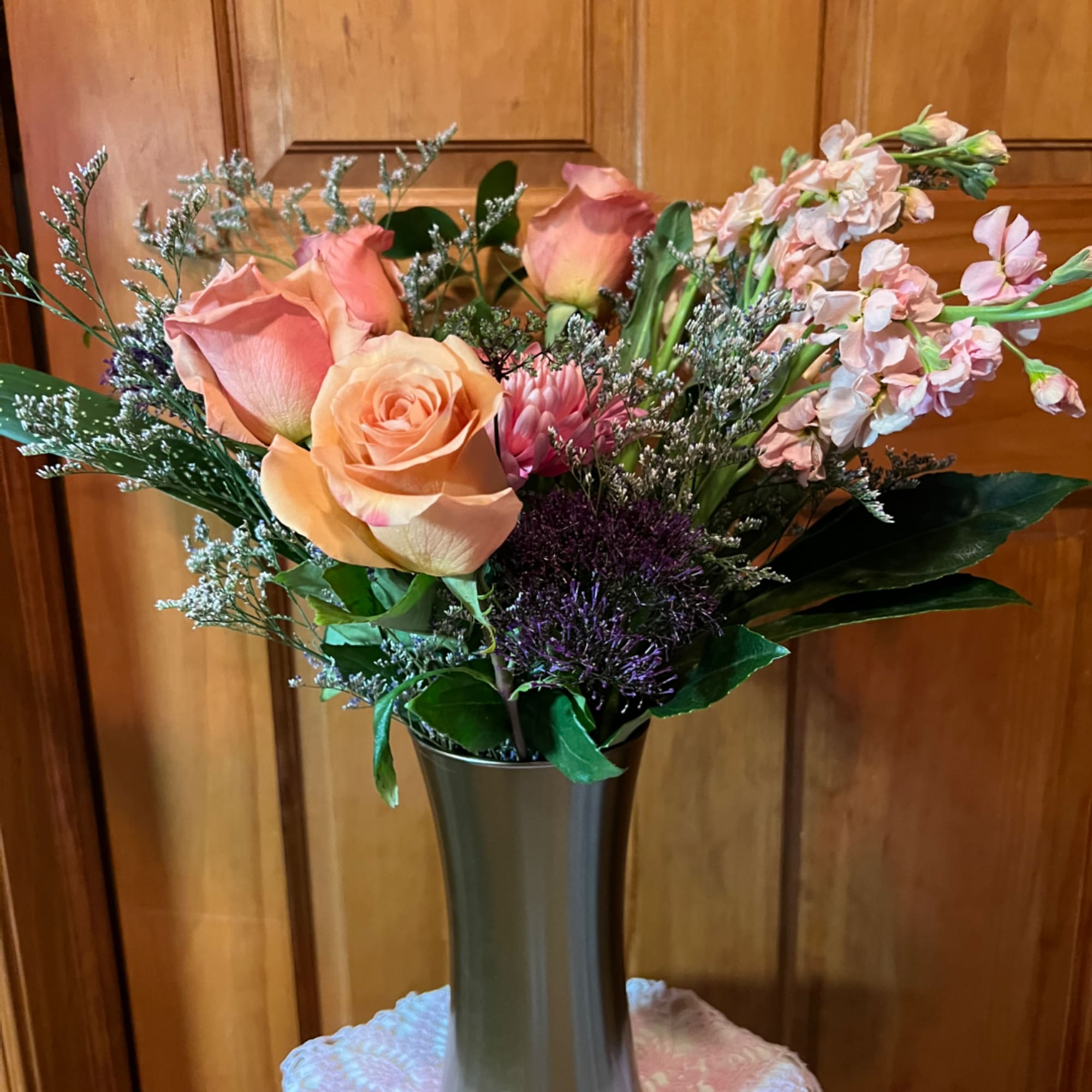 Peach and pink roses with purple filler flowers in a tall vase