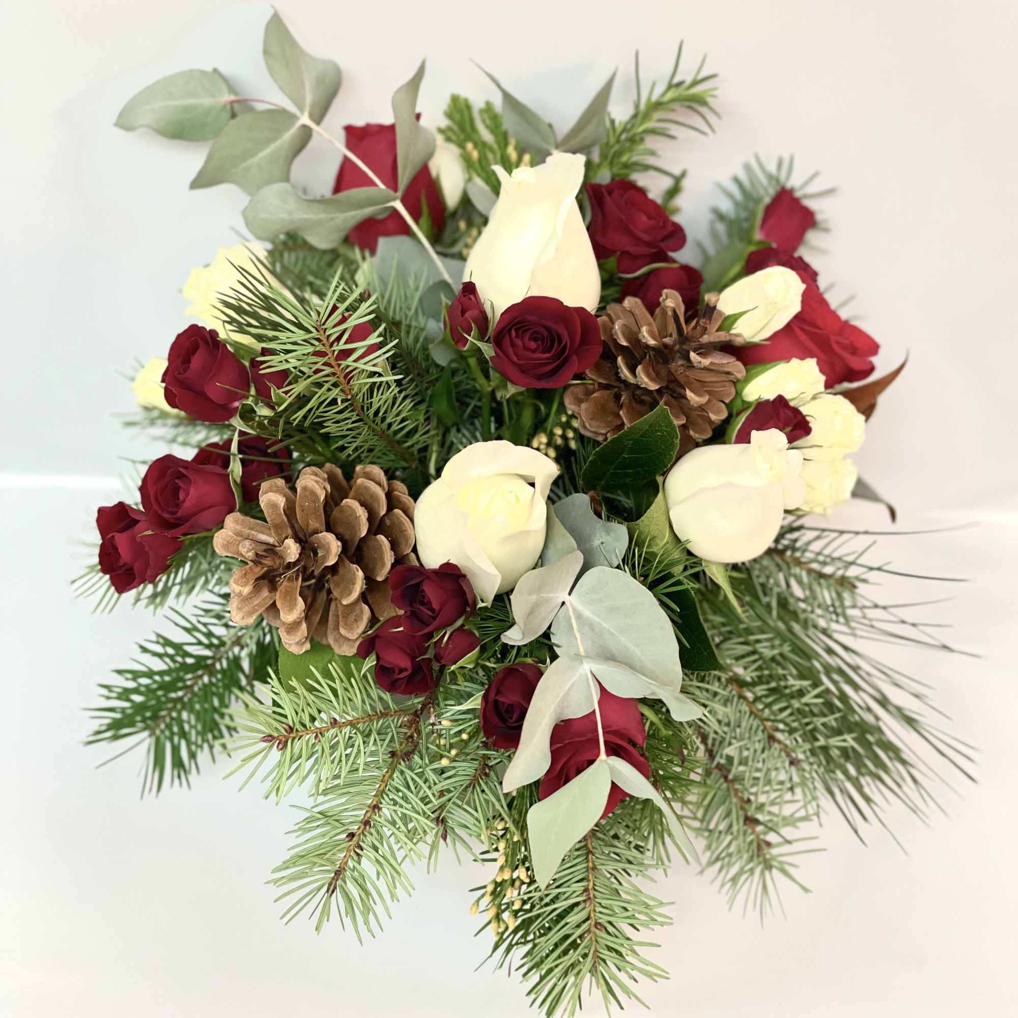 Bouquet of red and white roses with pinecones and evergreen branches