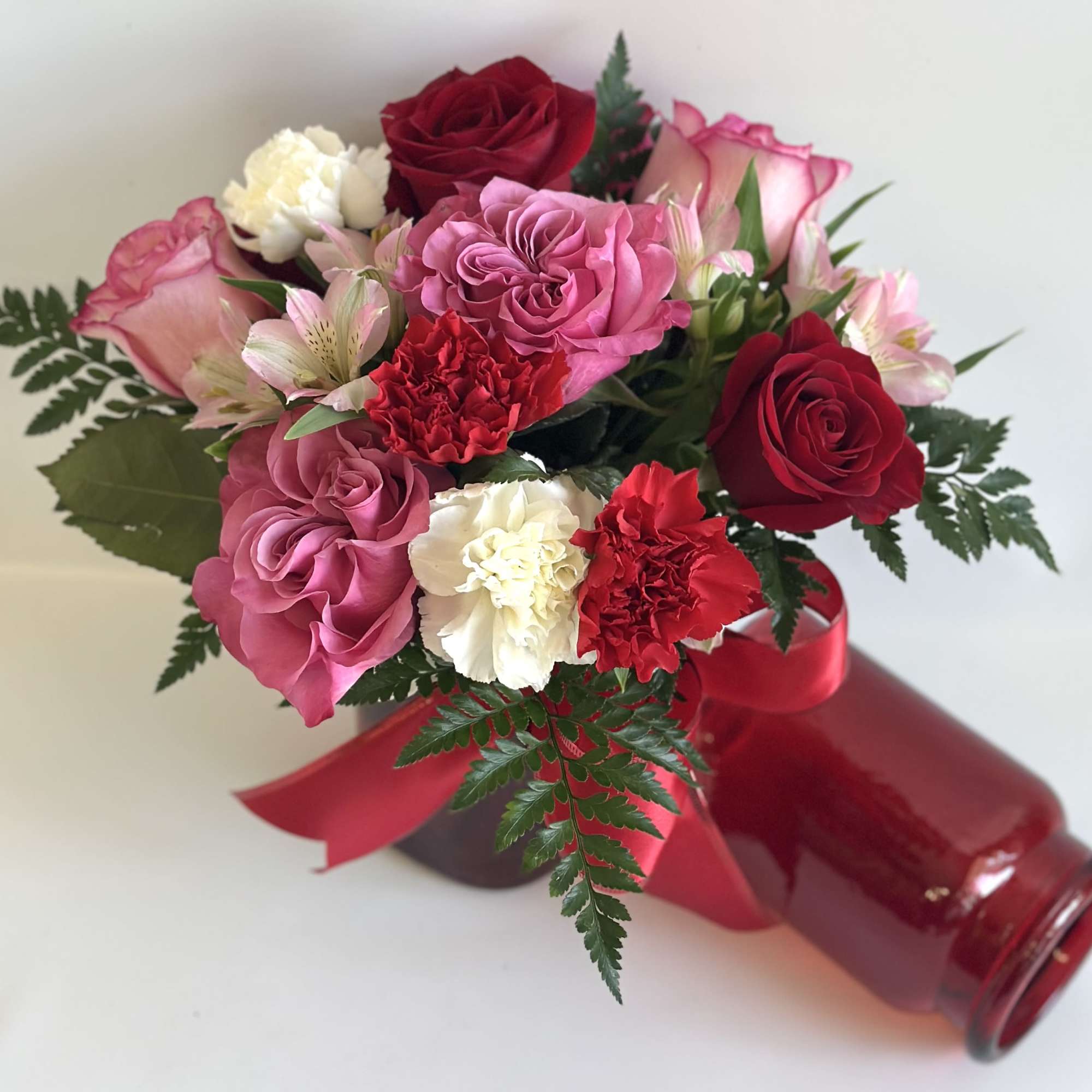 Bouquet of pink and red flowers in a red glass vase with ribbon