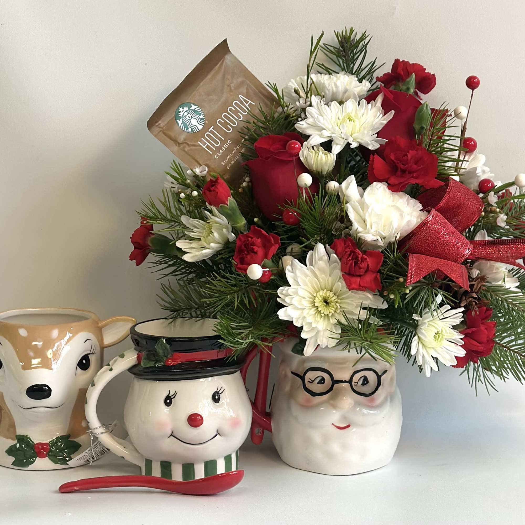 Holiday floral arrangement in a Santa mug with red and white flowers