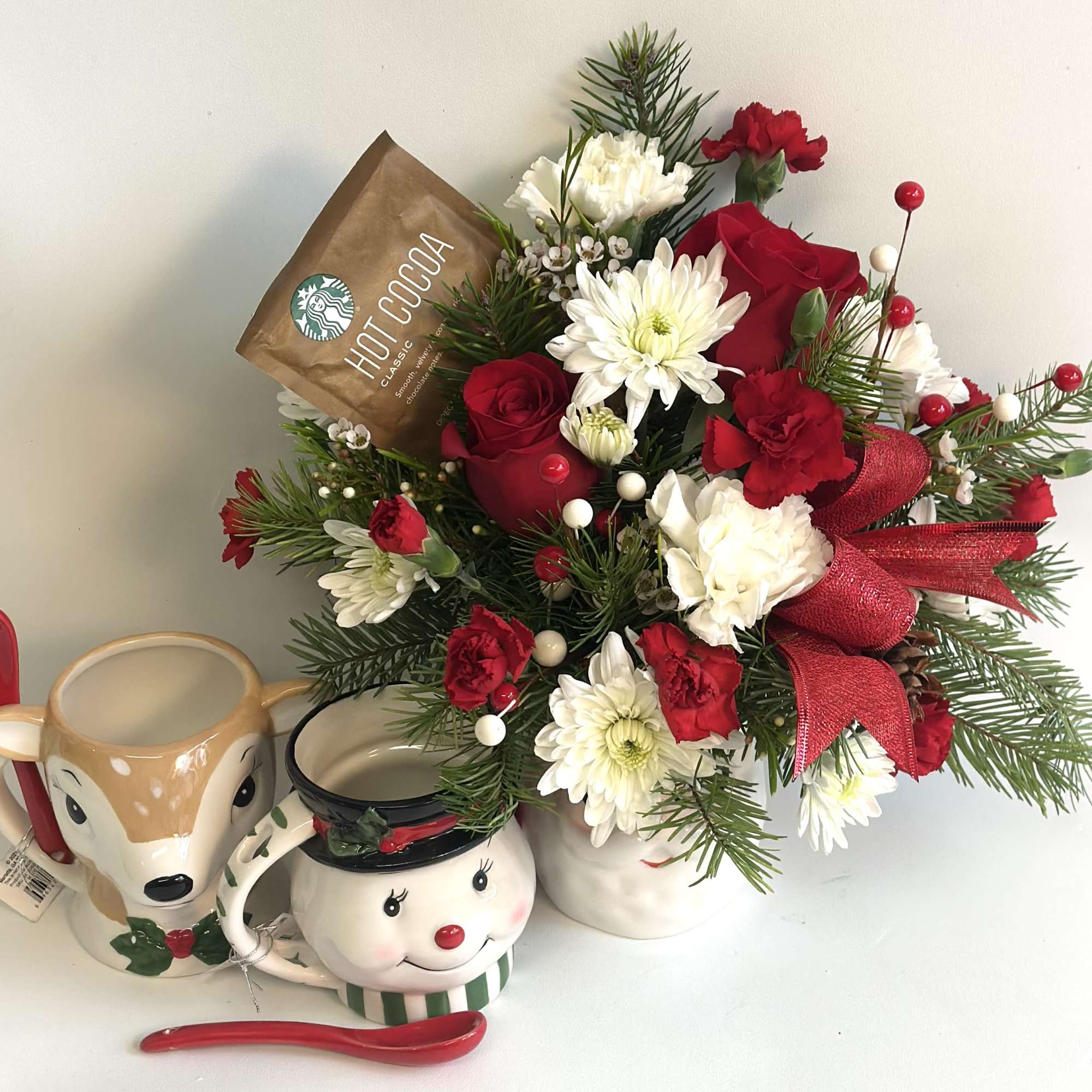 Holiday bouquet with red and white flowers in a white container beside festive mugs