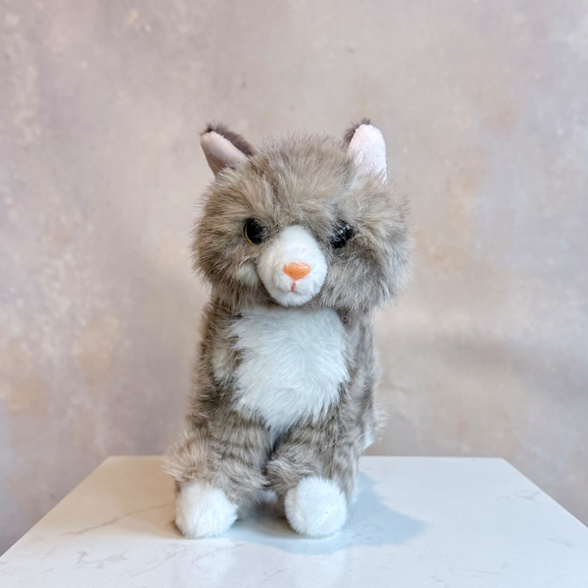 Small gray-and-white plush cat sitting on a tabletop