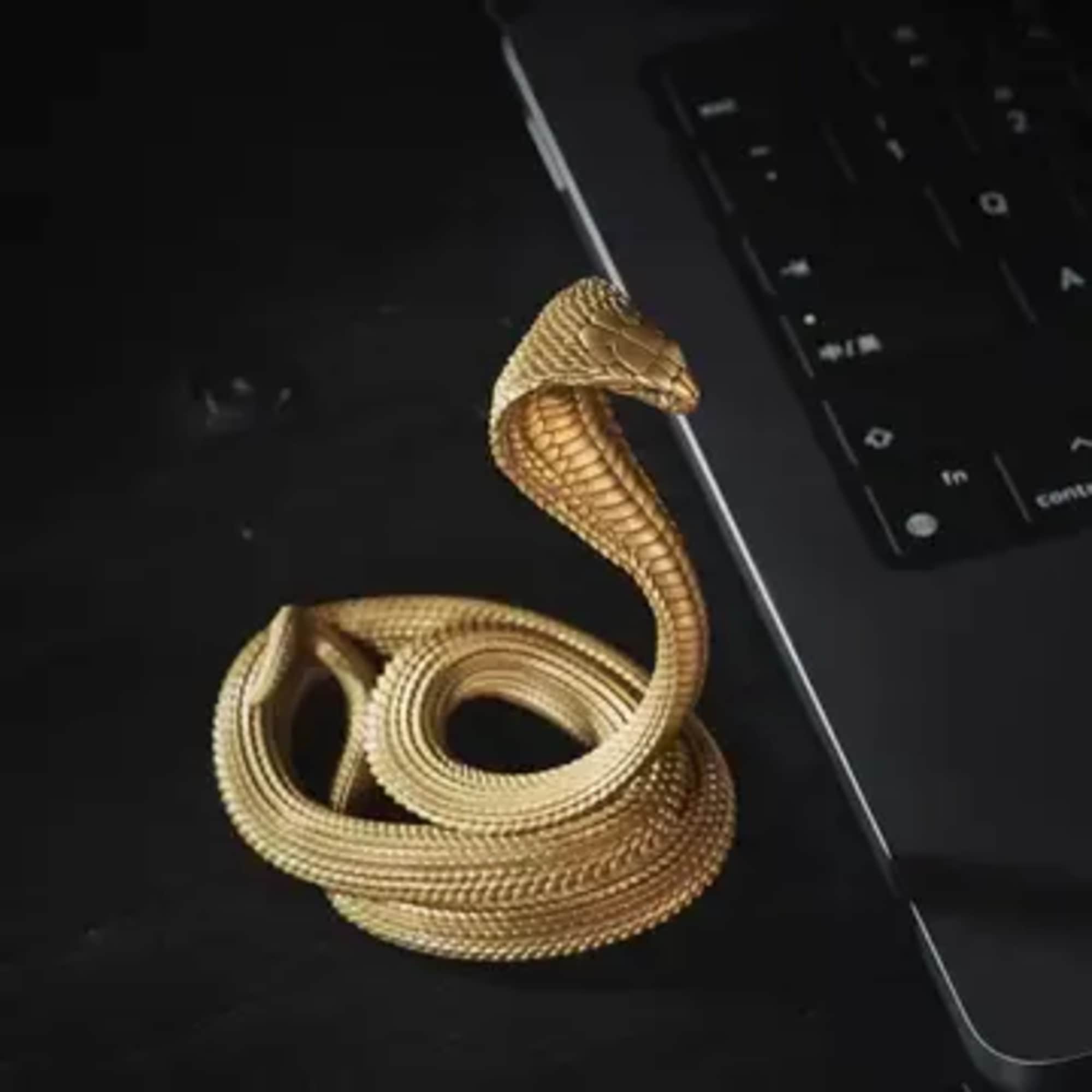 Gold cobra-shaped ring on a dark surface beside a keyboard