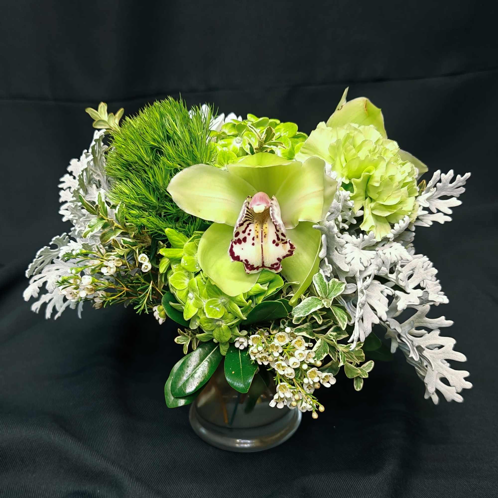 Green orchid arrangement in a clear glass vase with white foliage accents