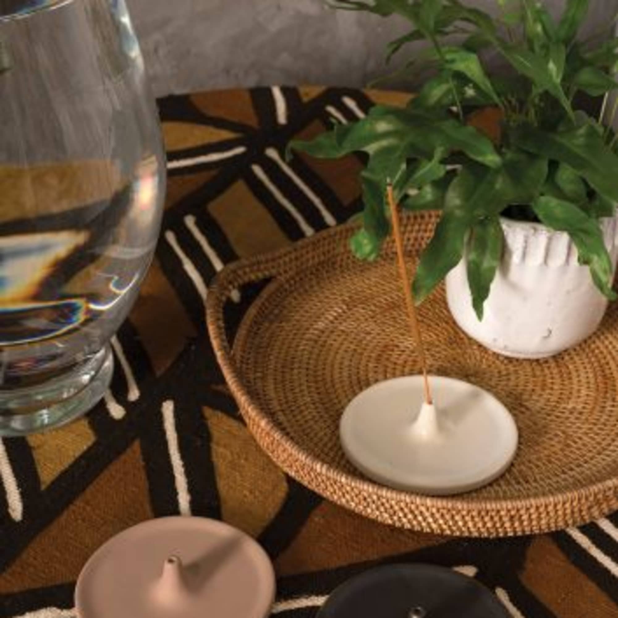 Potted green plant in a white container beside a glass of water and candles