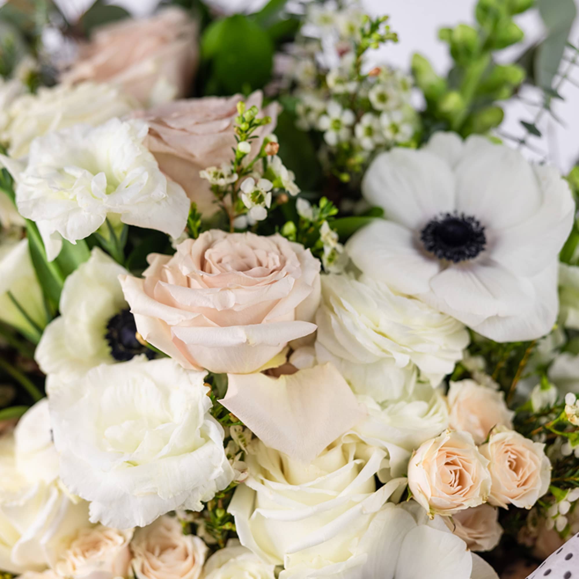 Close-up of a bouquet with blush roses, white anemones, and other soft white flowers.