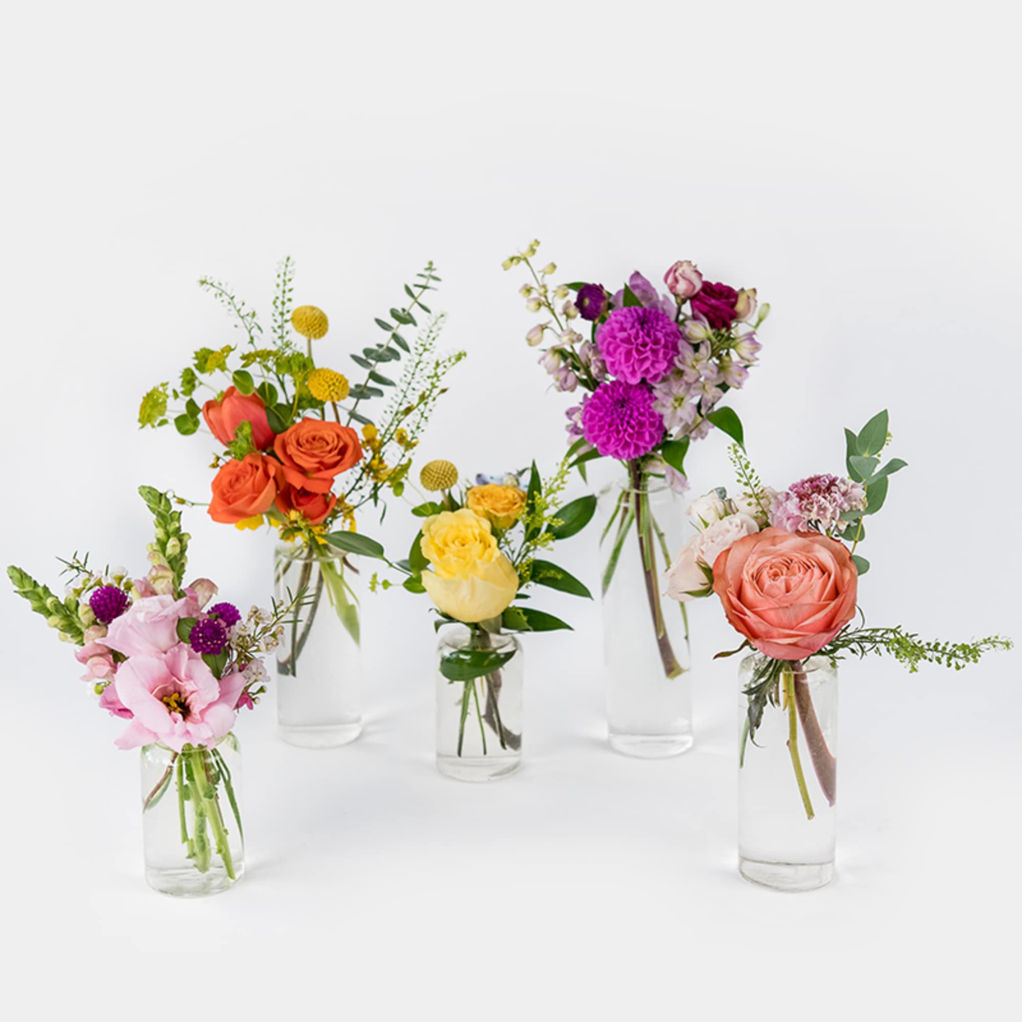 Five small mixed flower arrangements in clear glass bud vases on a white background