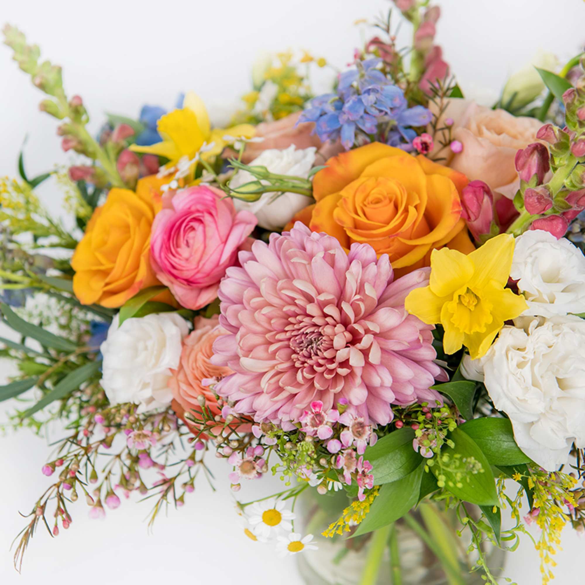 Colorful mixed bouquet of pink mum, roses, daffodils, and other blooms in a clear glass vase