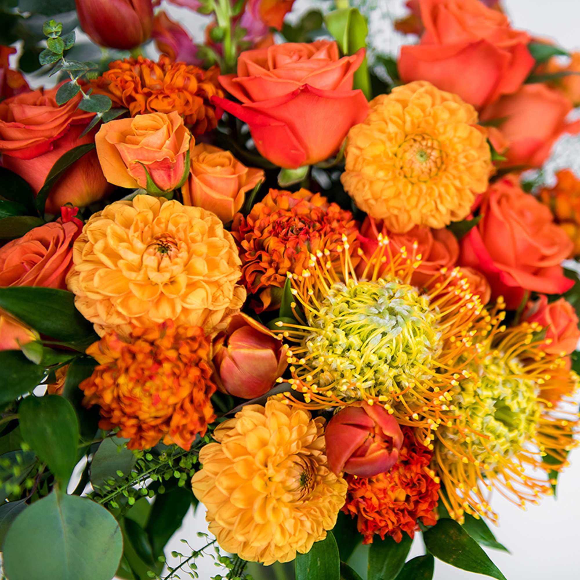 Bouquet of bright orange roses, yellow pincushion protea, and round orange blooms