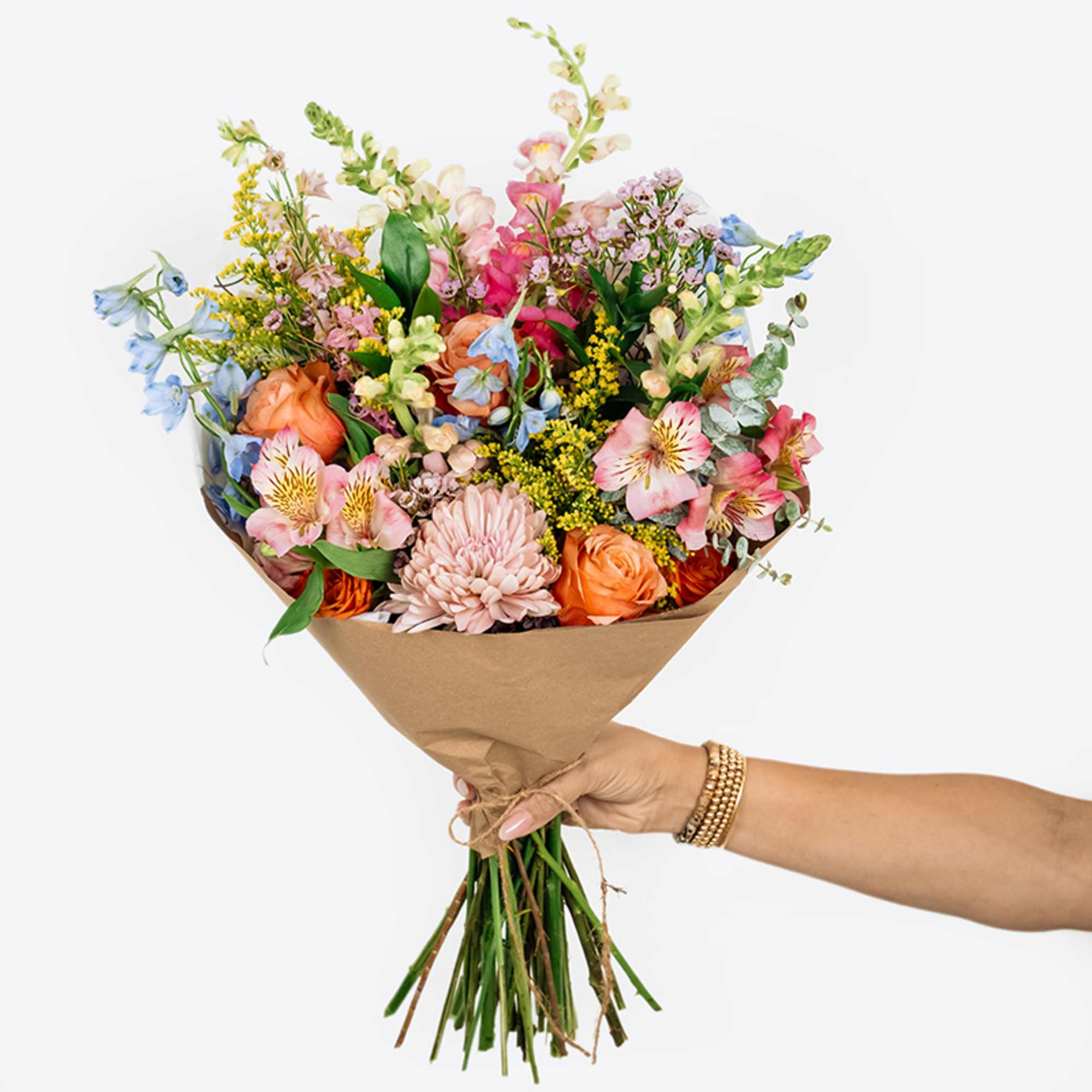 Handheld bouquet of mixed pastel flowers wrapped in brown paper