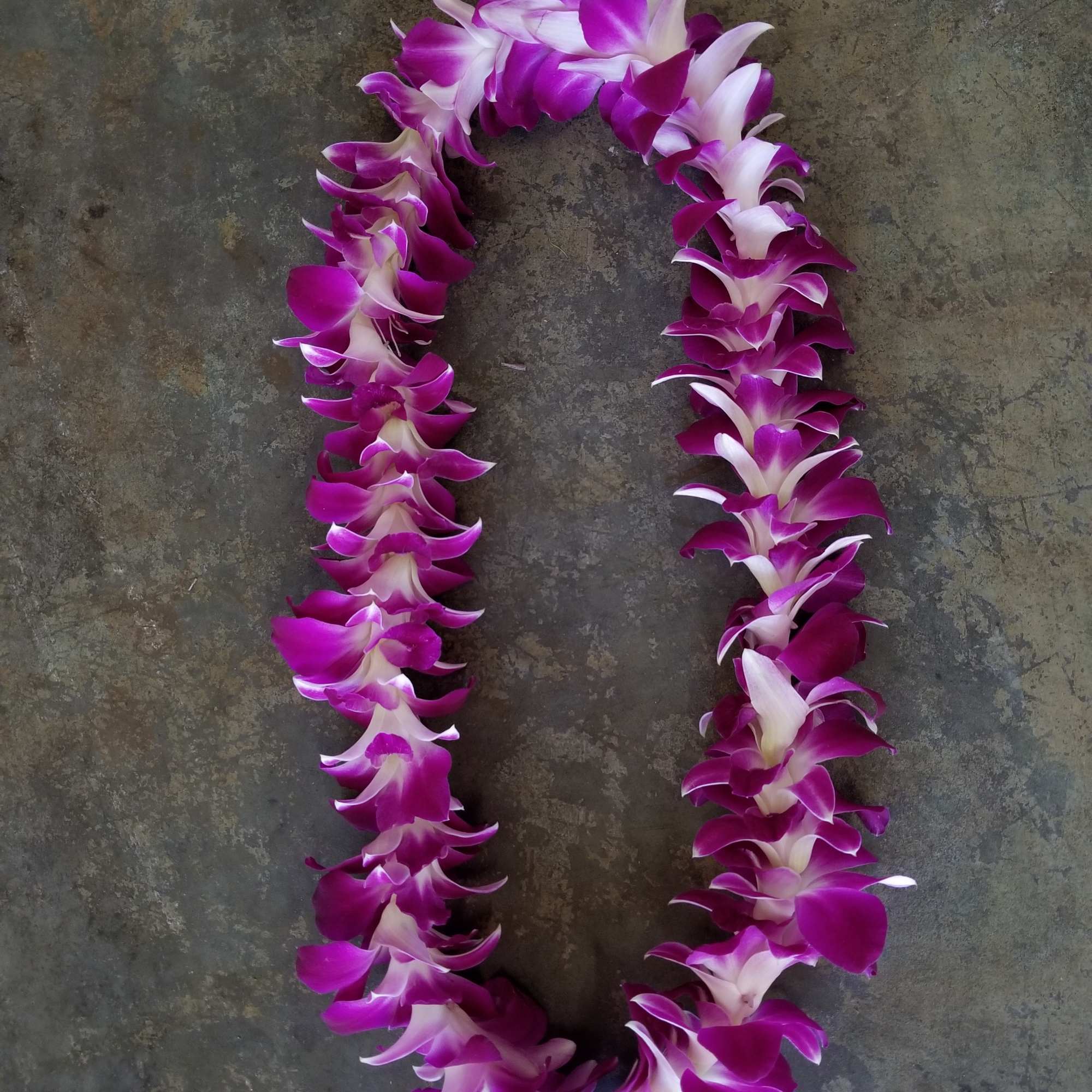 Purple and white orchid lei on a dark stone surface