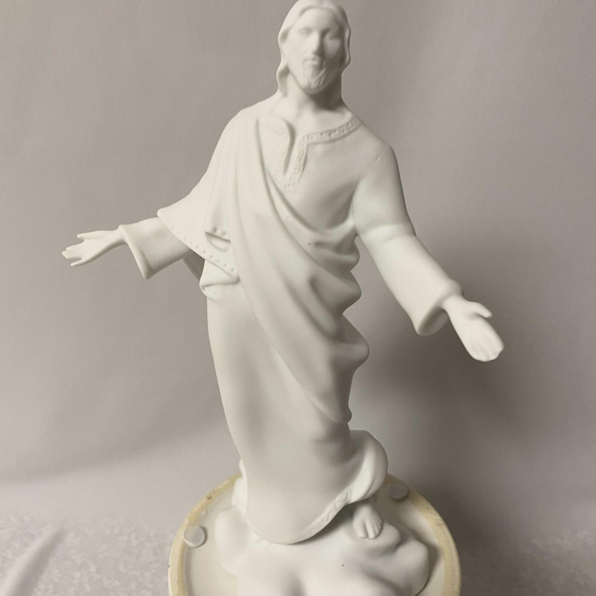 White religious statue of Jesus with outstretched arms on a round base