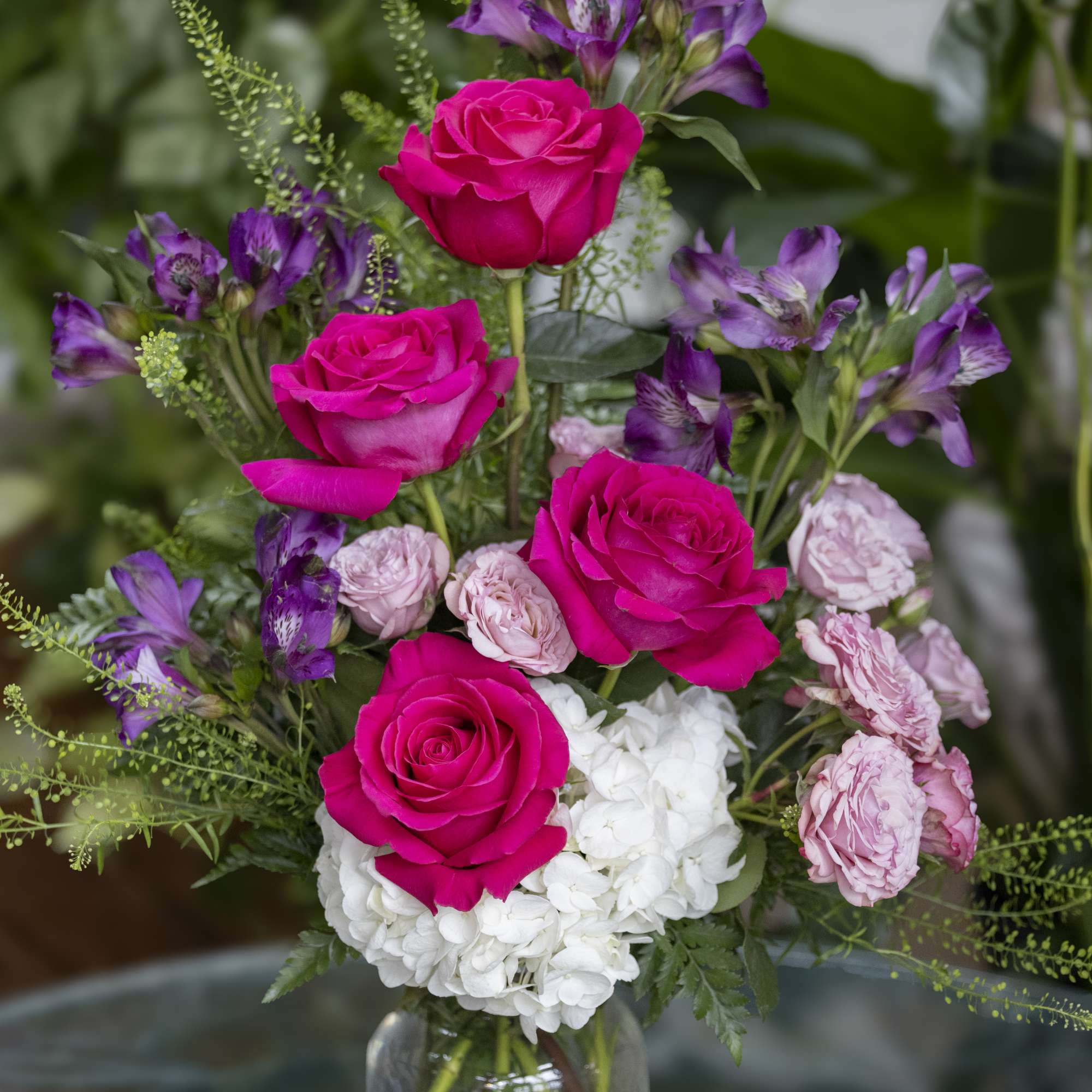Bouquet of hot pink roses, purple alstroemeria, and white hydrangea in a glass vase
