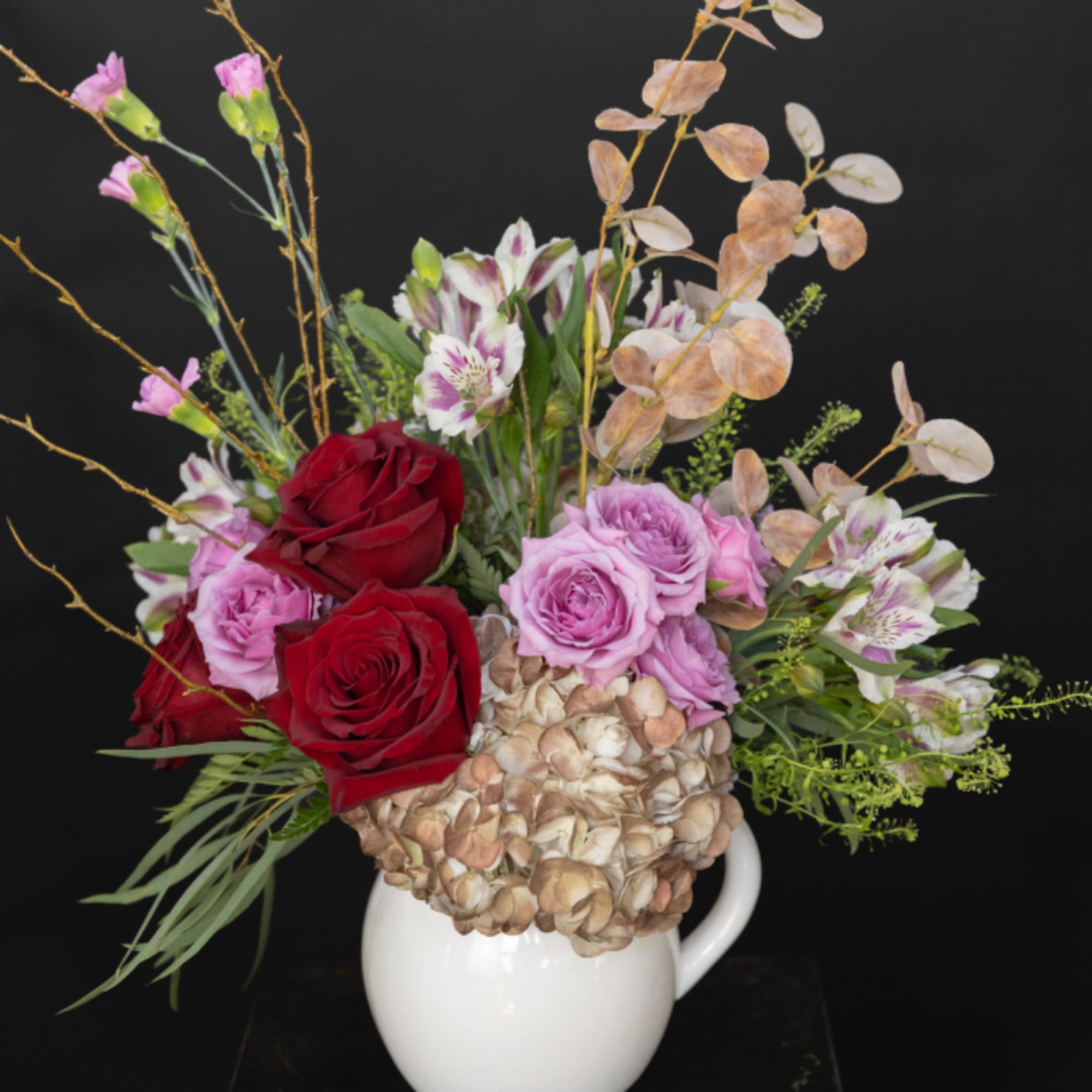 Bouquet of red and lavender roses with alstroemeria in a white pitcher vase