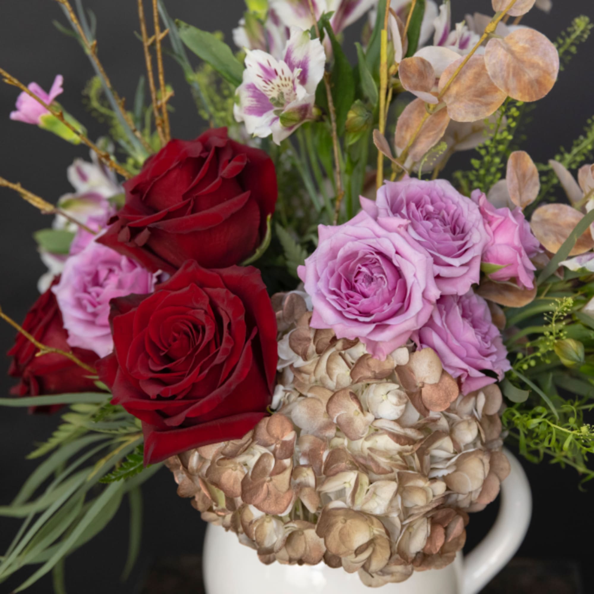 Mixed bouquet of red and lavender roses with hydrangea in a white pitcher