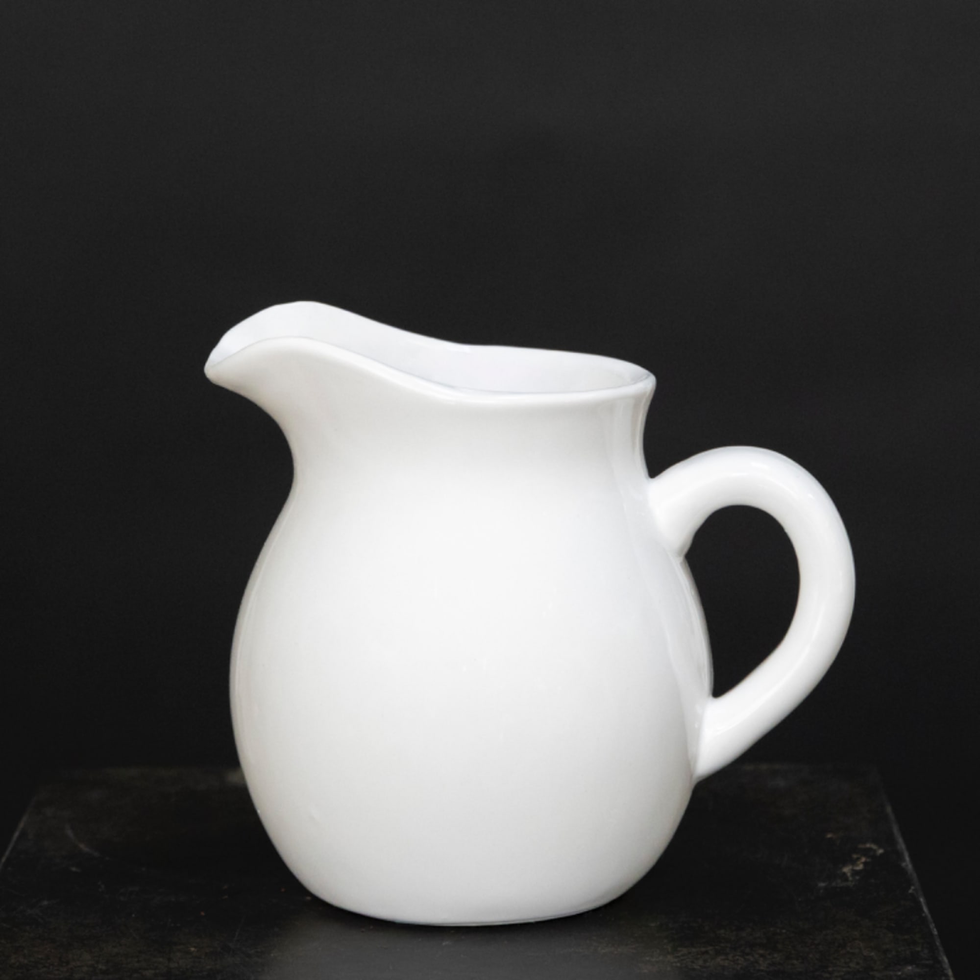 White ceramic pitcher on a dark surface against a black background