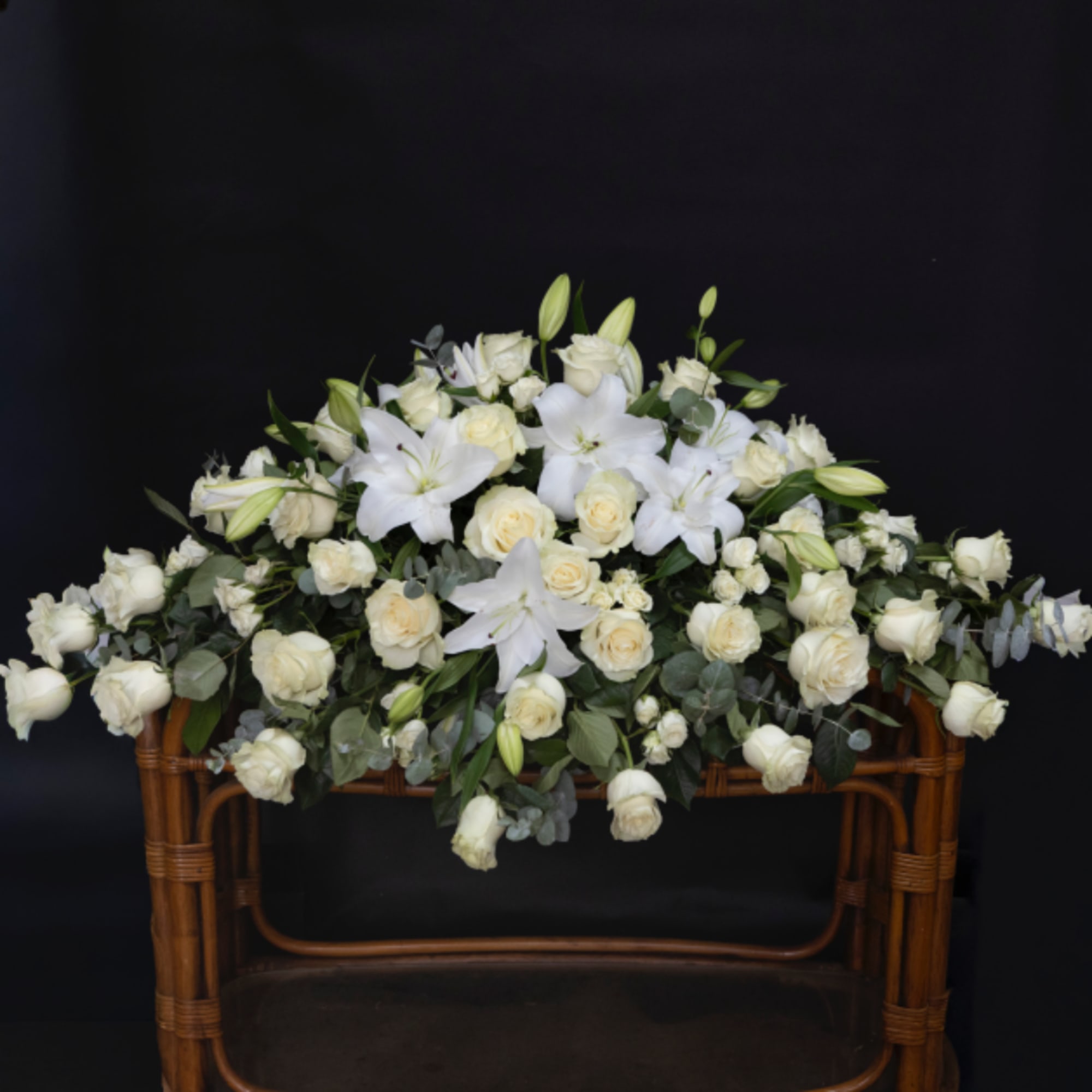 White roses and lilies arranged on a wicker stand