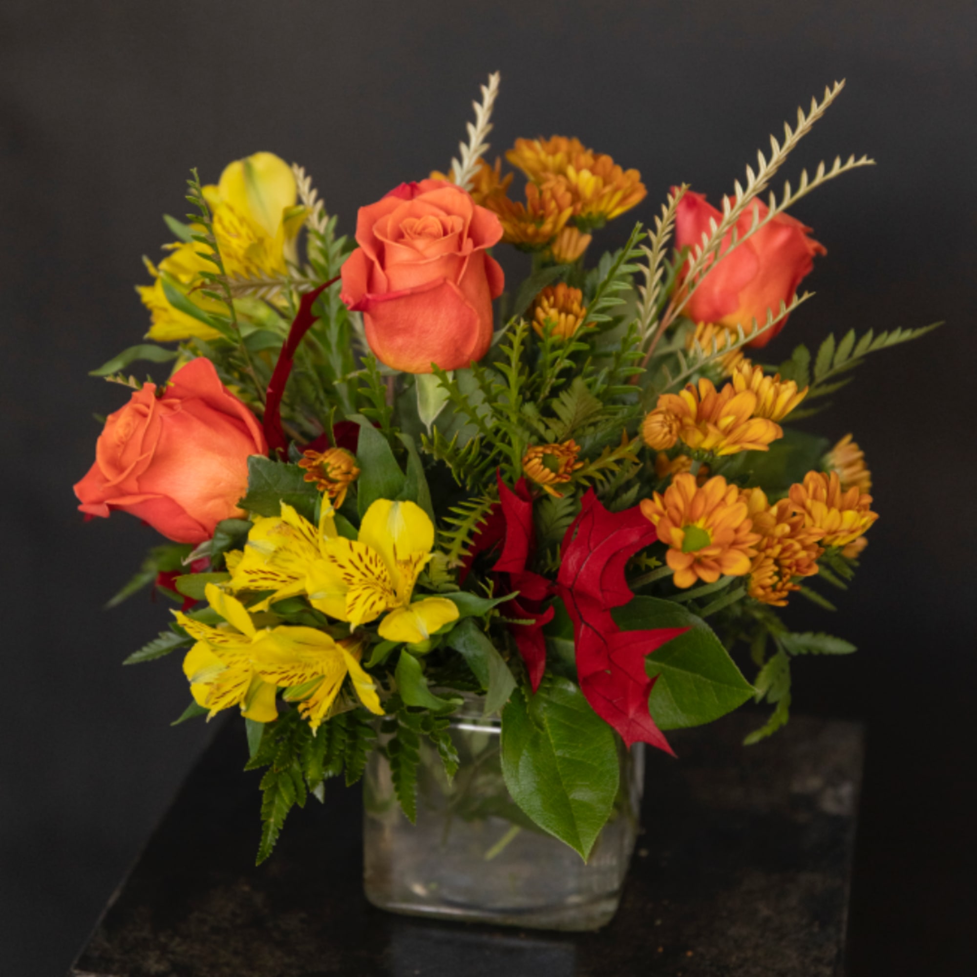 Orange roses and yellow flowers in a clear square vase