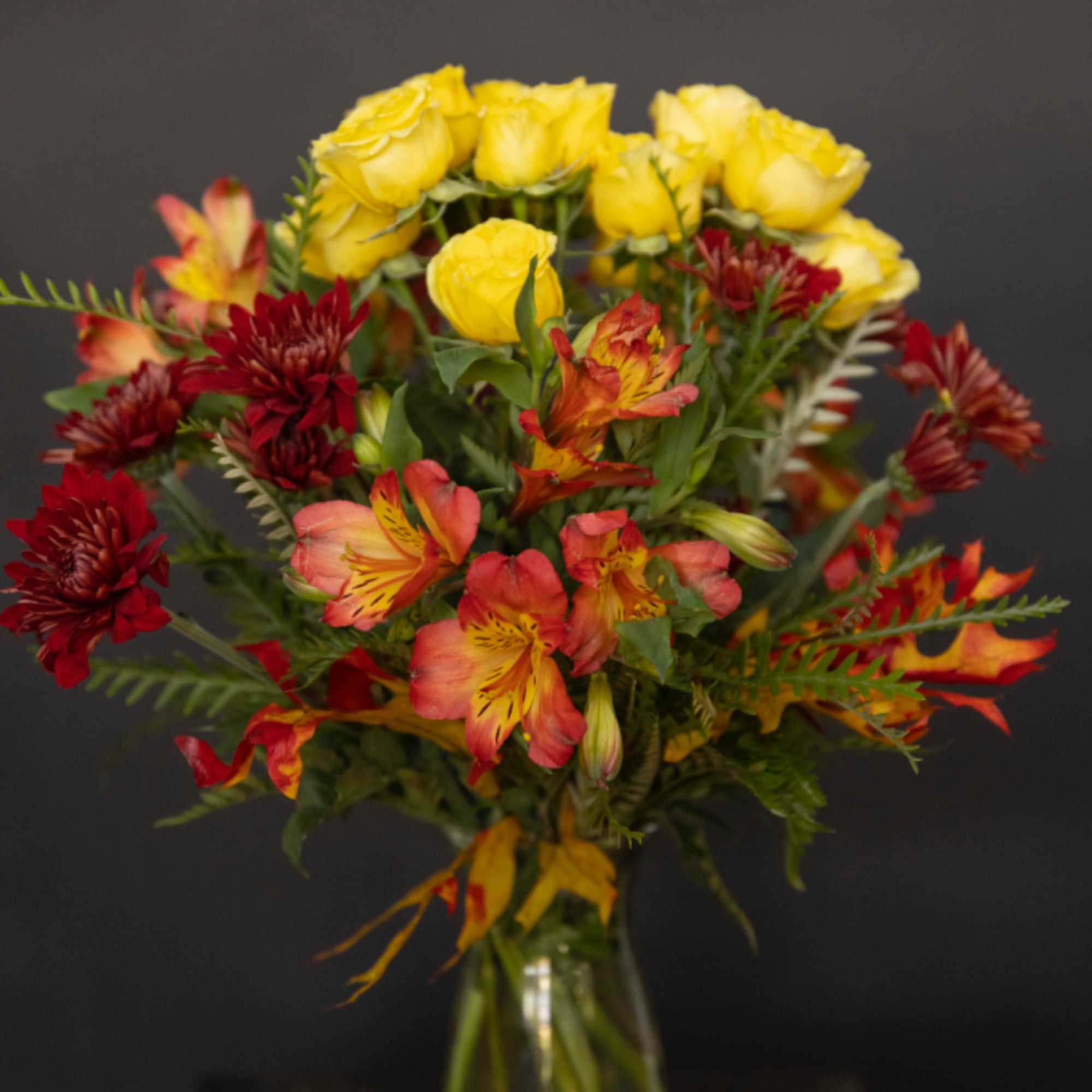 Bouquet of yellow roses and red-orange flowers in a glass vase