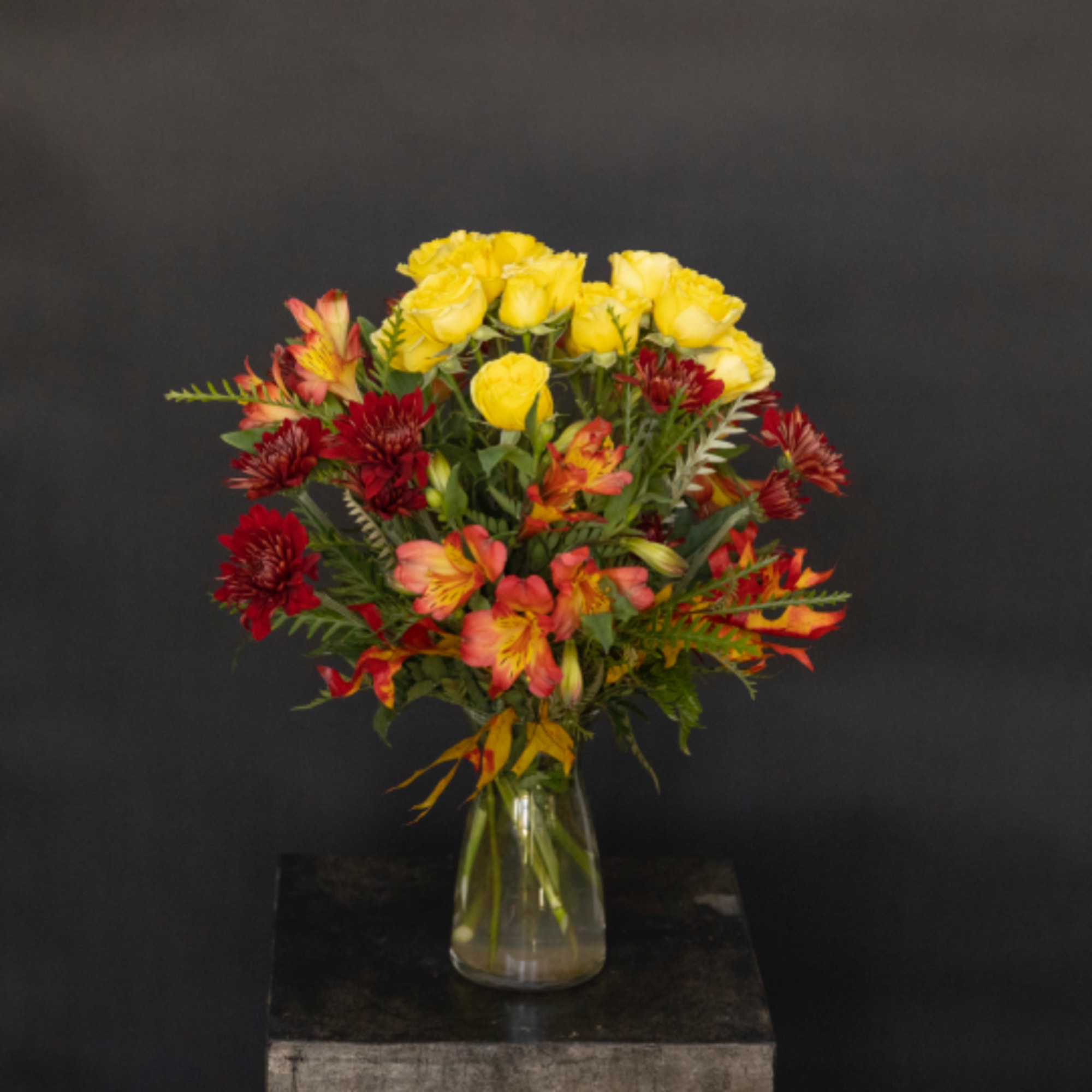 Yellow roses and red alstroemeria in a clear glass vase