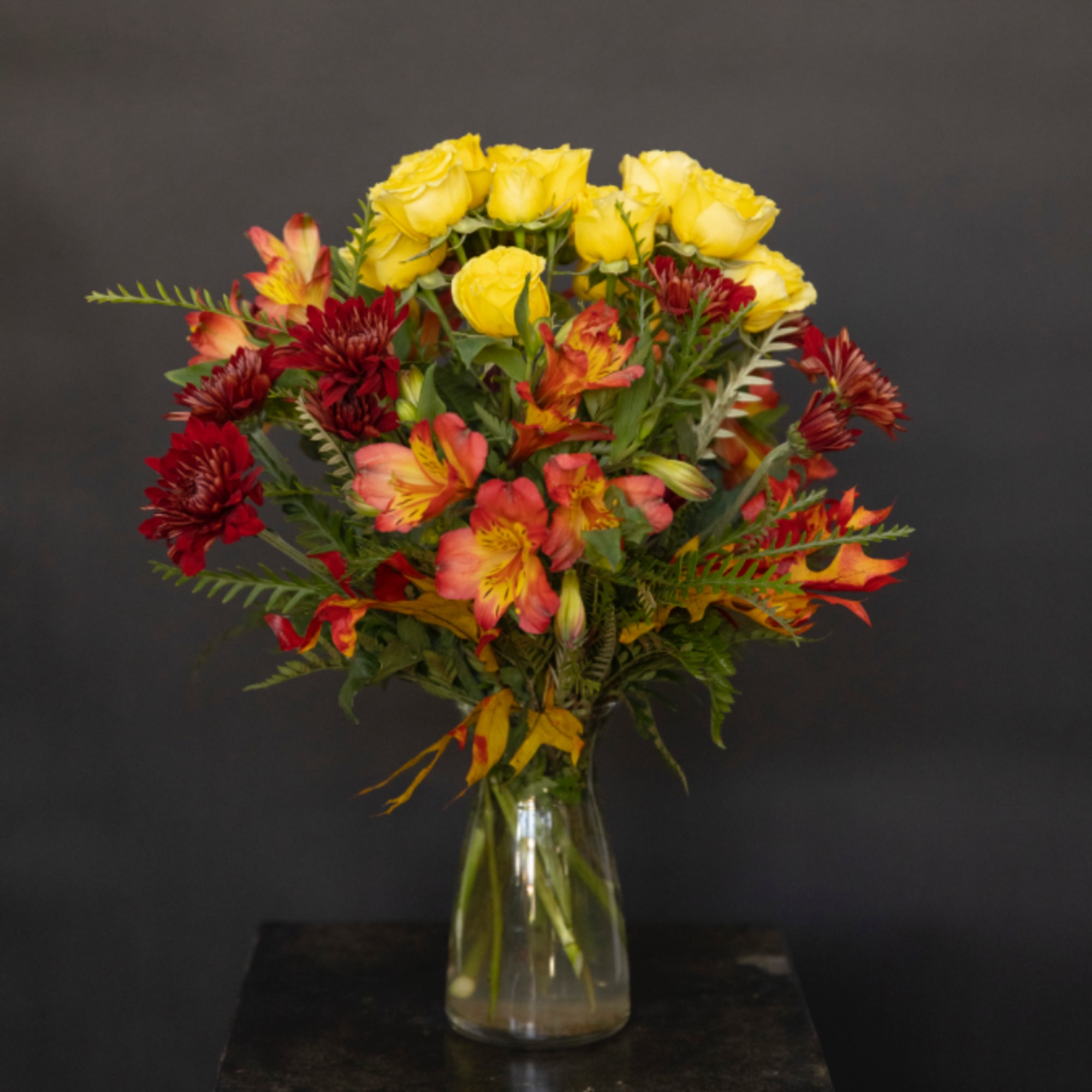 Bouquet of yellow roses and red-orange flowers in a clear glass vase