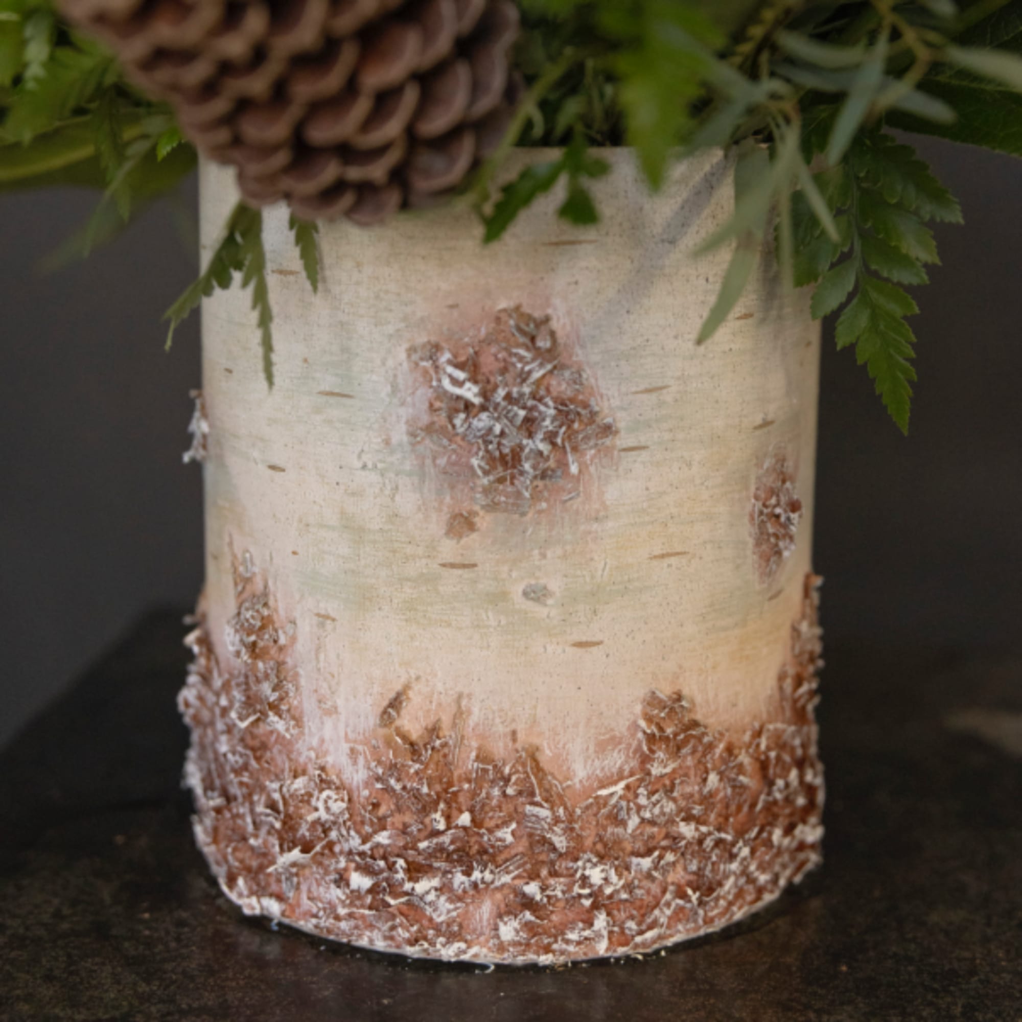 Birch bark vase with greenery and a pinecone accent