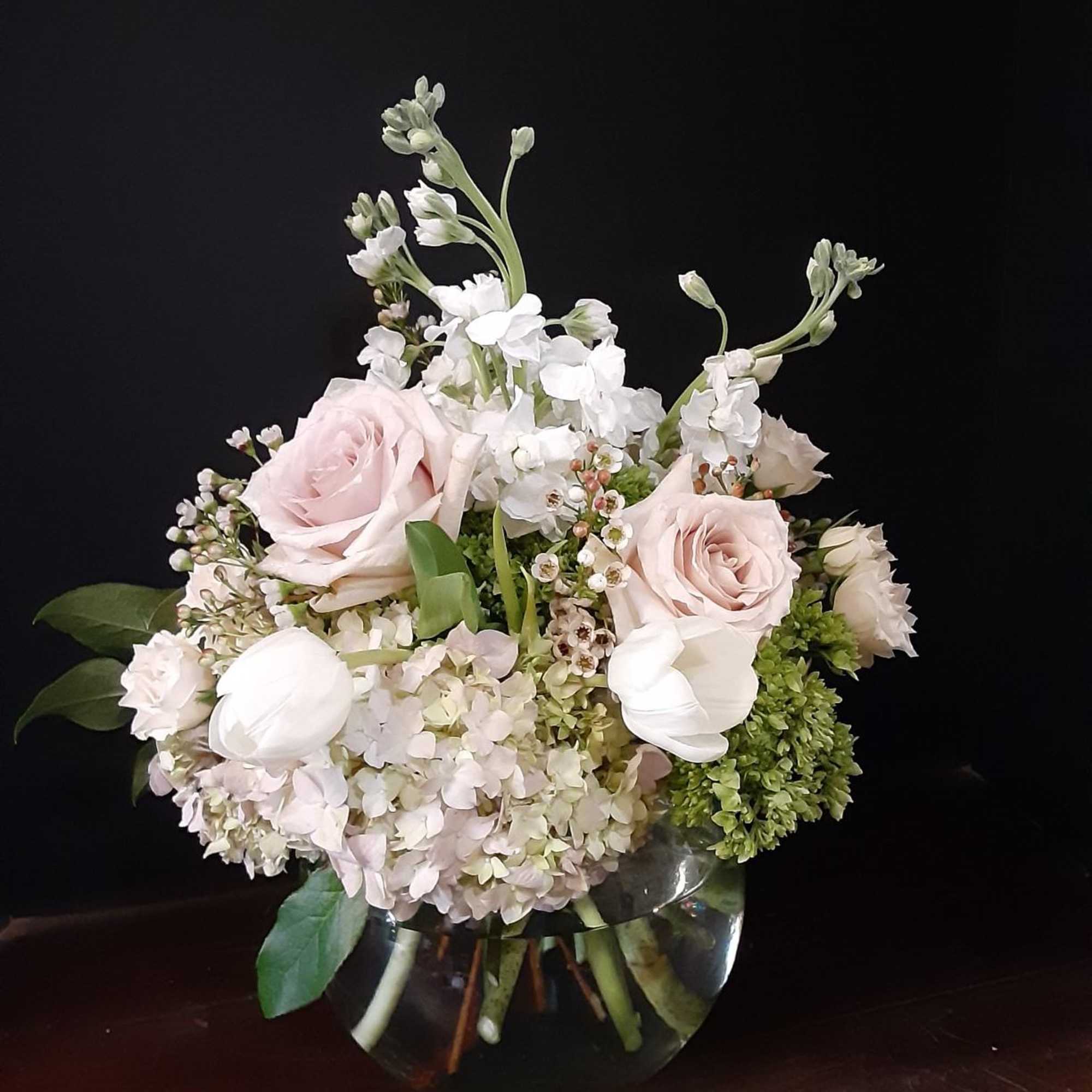 Soft pink roses and white flowers arranged in a clear glass vase