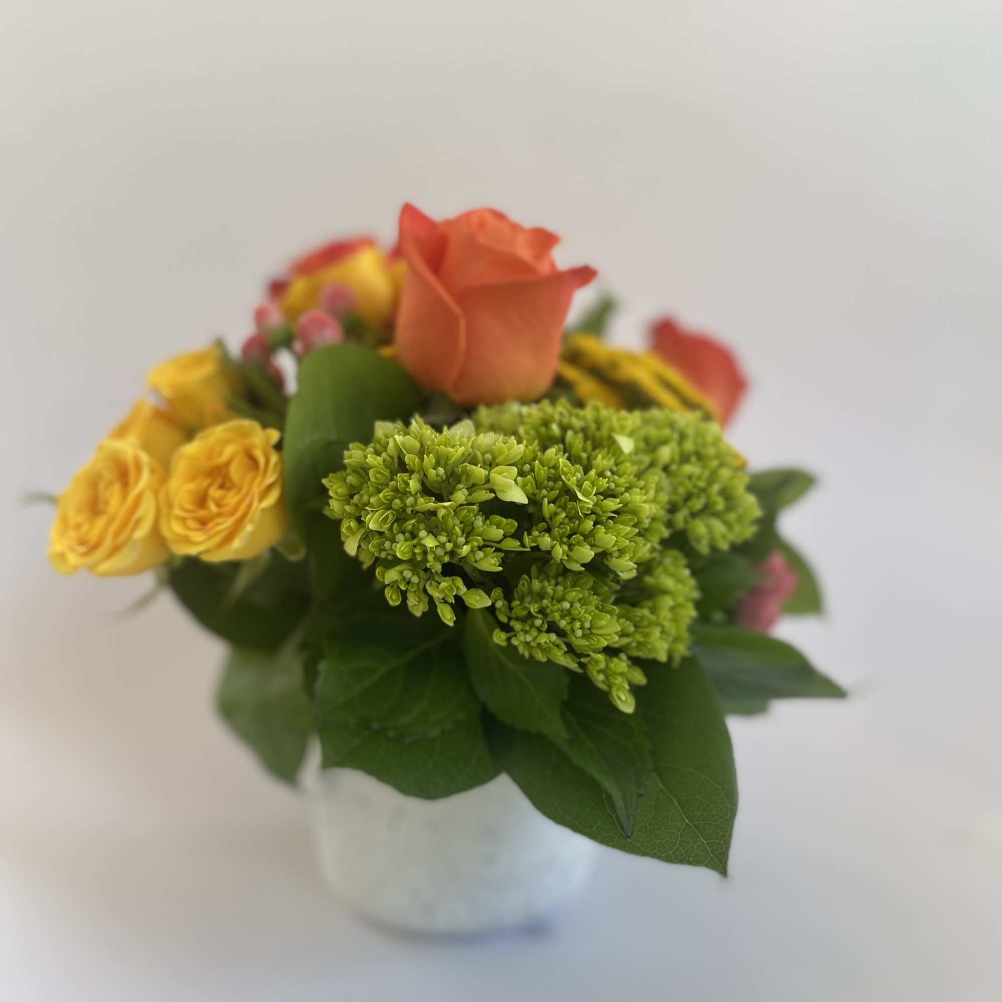 Small bouquet of orange and yellow roses in a white vase